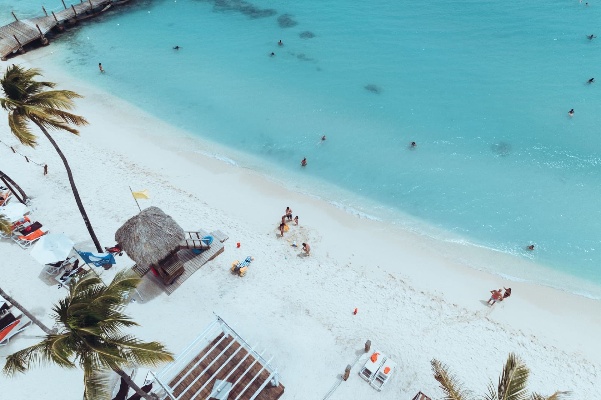 Aerial view of a tropical beach with palm trees and swimmers enjoying clear turquoise waters.