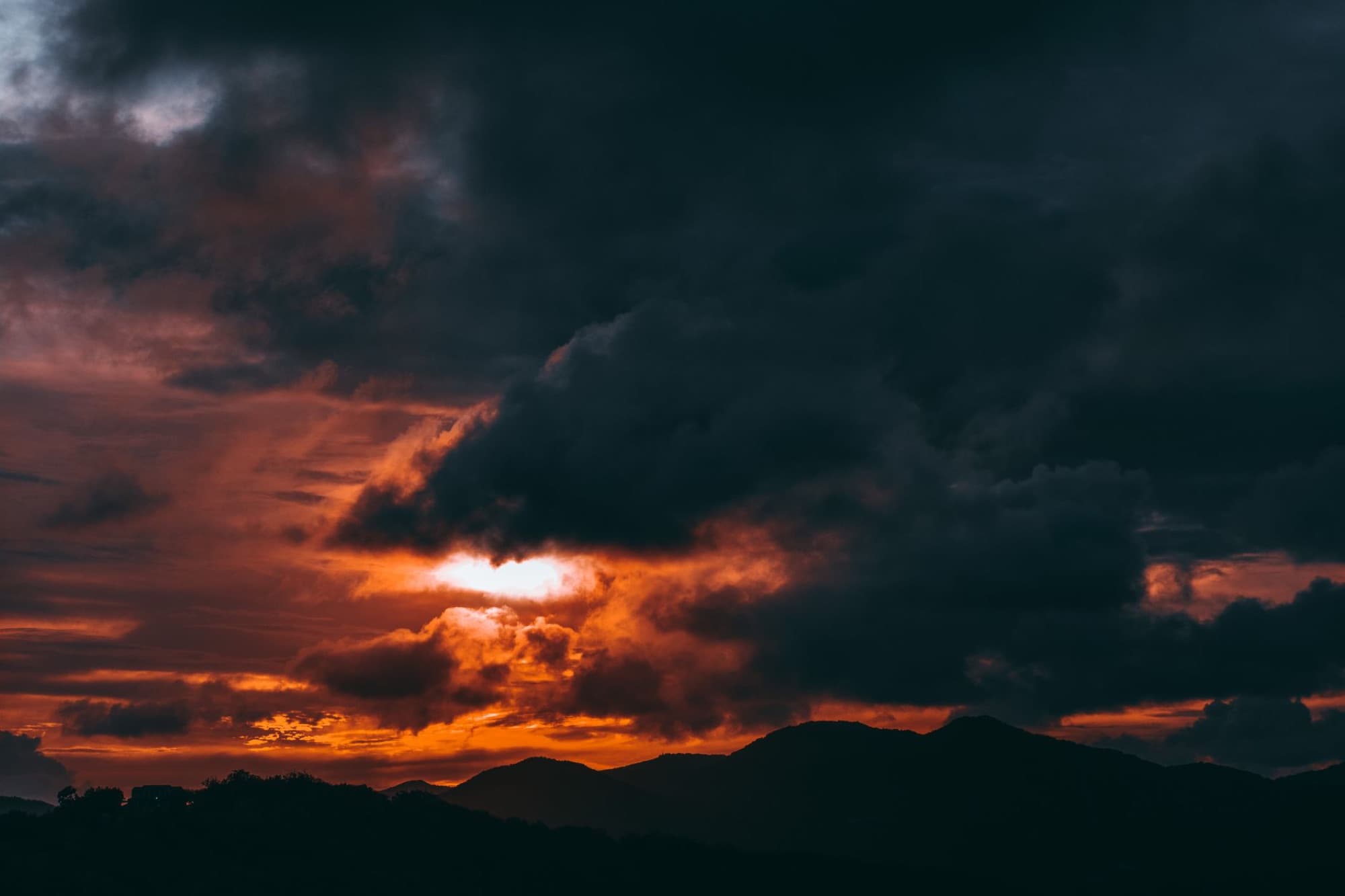 A stunning sunset with dark clouds over mountains in Antigua and Barbuda, creating a vibrant and moody scene.