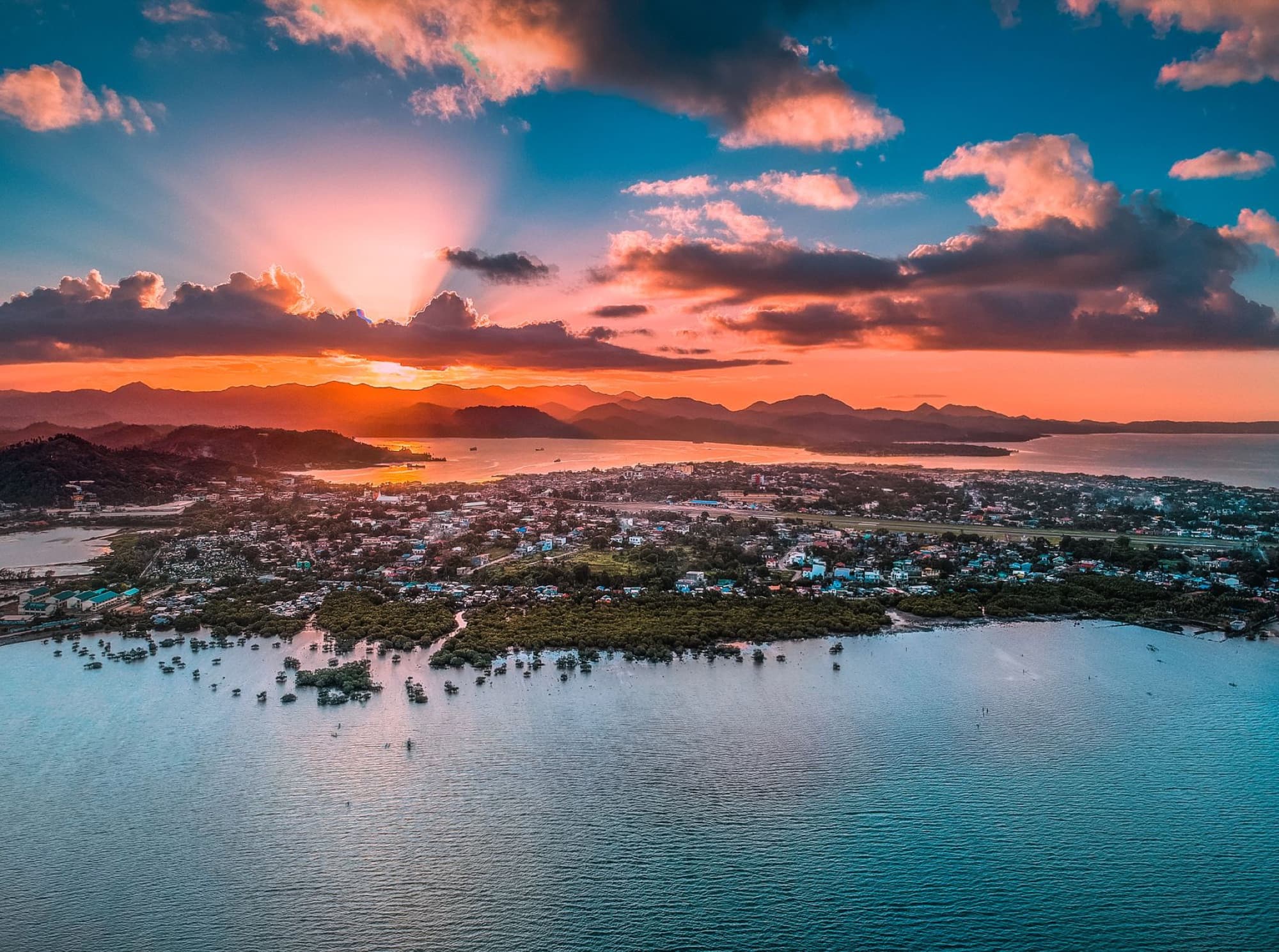 A breathtaking aerial view of a coastal town at sunrise with vibrant skies and serene waters.