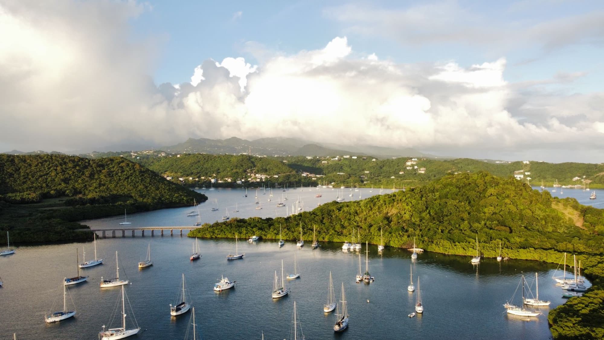 Aerial view of sailboats on a lake surrounded by lush green mountains under a cloudy sky.
