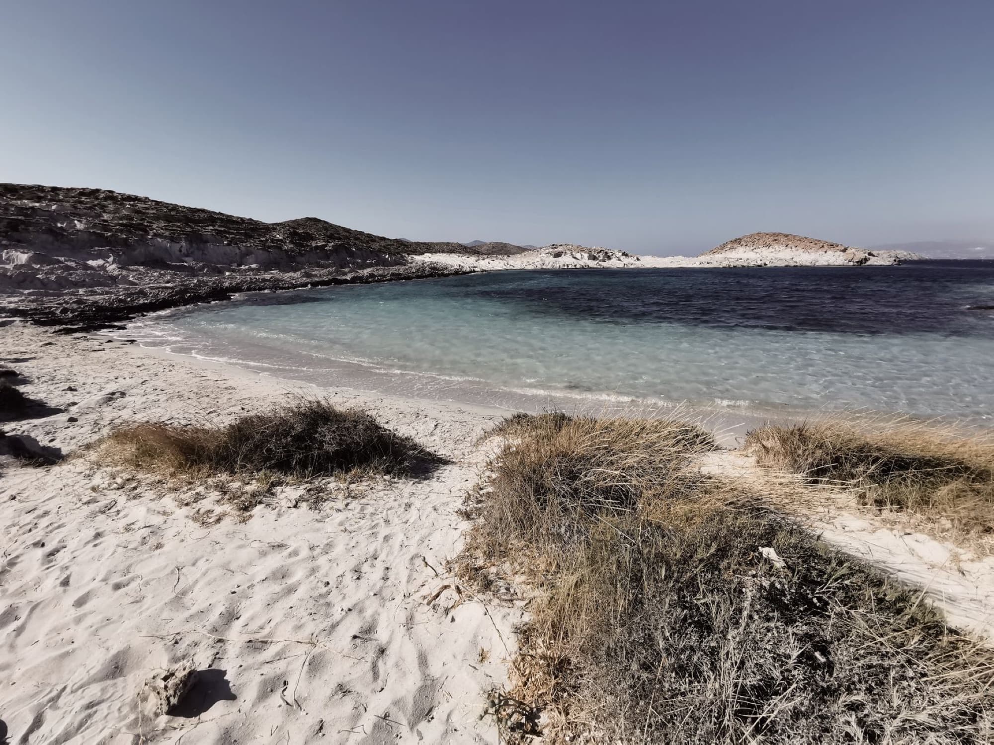 Tranquil beach in Antiparos, Greece with crystal clear water under a bright summer sky.