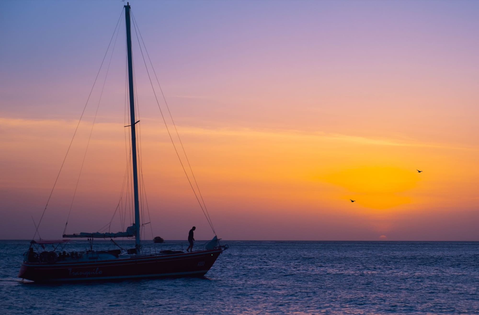 A tranquil sailboat silhouette against a vibrant sunset over the sea in Aruba.