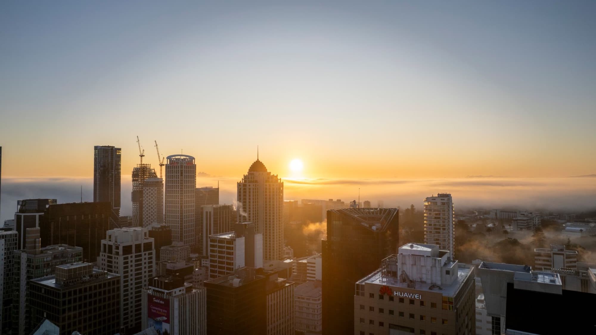 Stunning aerial view of Auckland skyline at sunrise with fog enveloping the city.