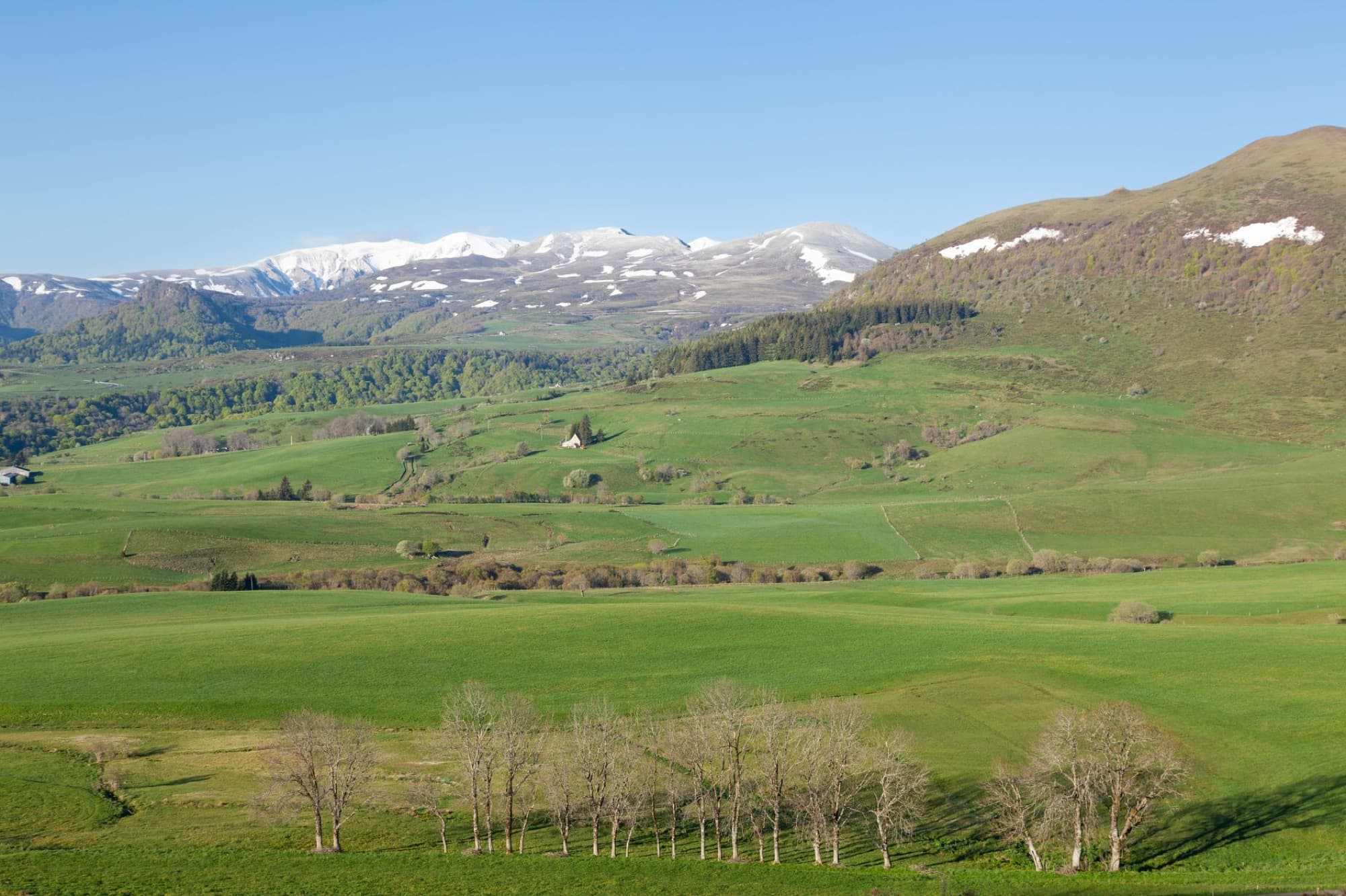 Scenic view of Mont-Dore in Auvergne-Rhône-Alpes, France with green hills and snowy peaks.