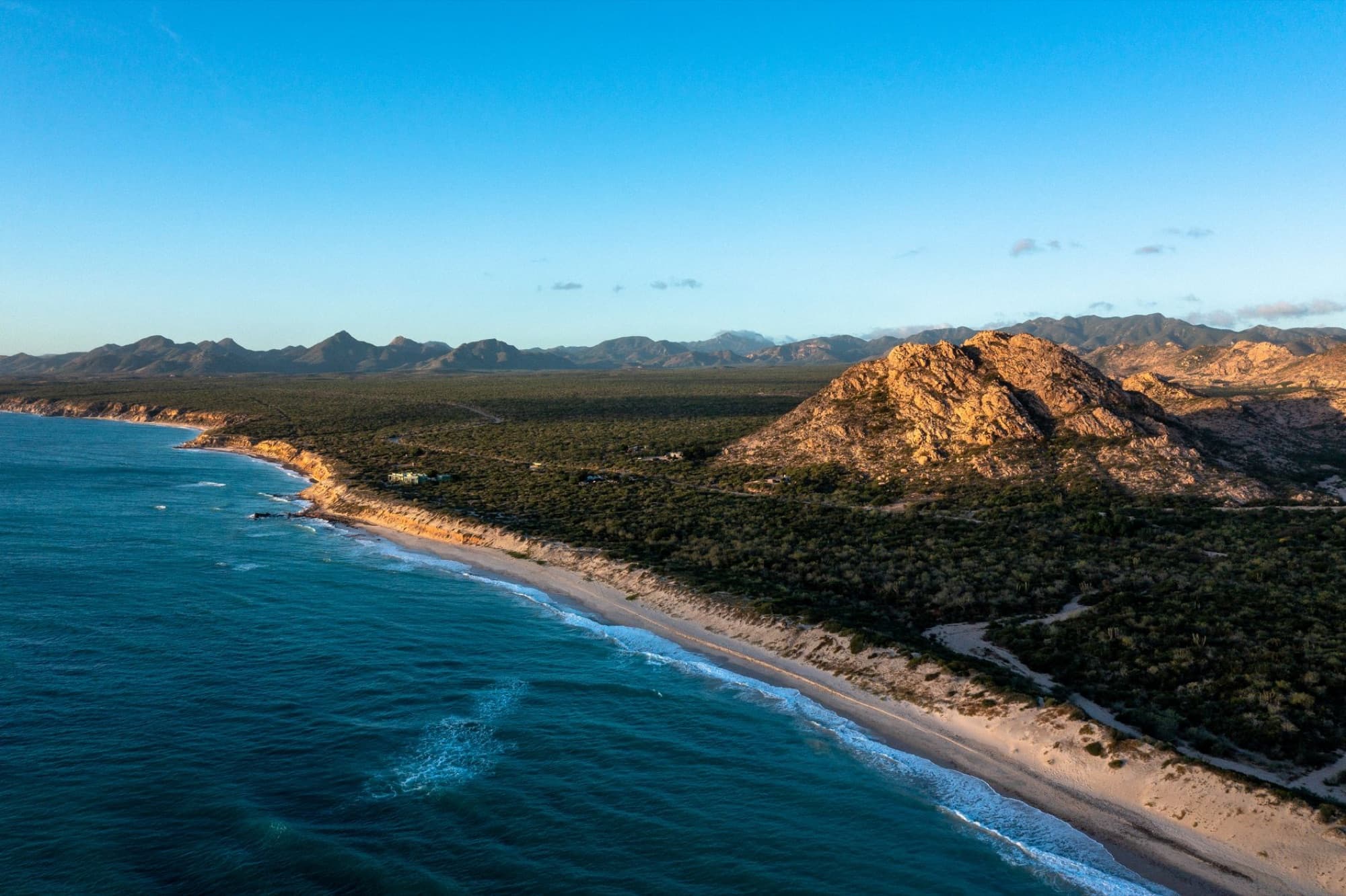 A breathtaking aerial view of Cabo Pulmo's rocky coastline and vibrant blue sea at sunrise.