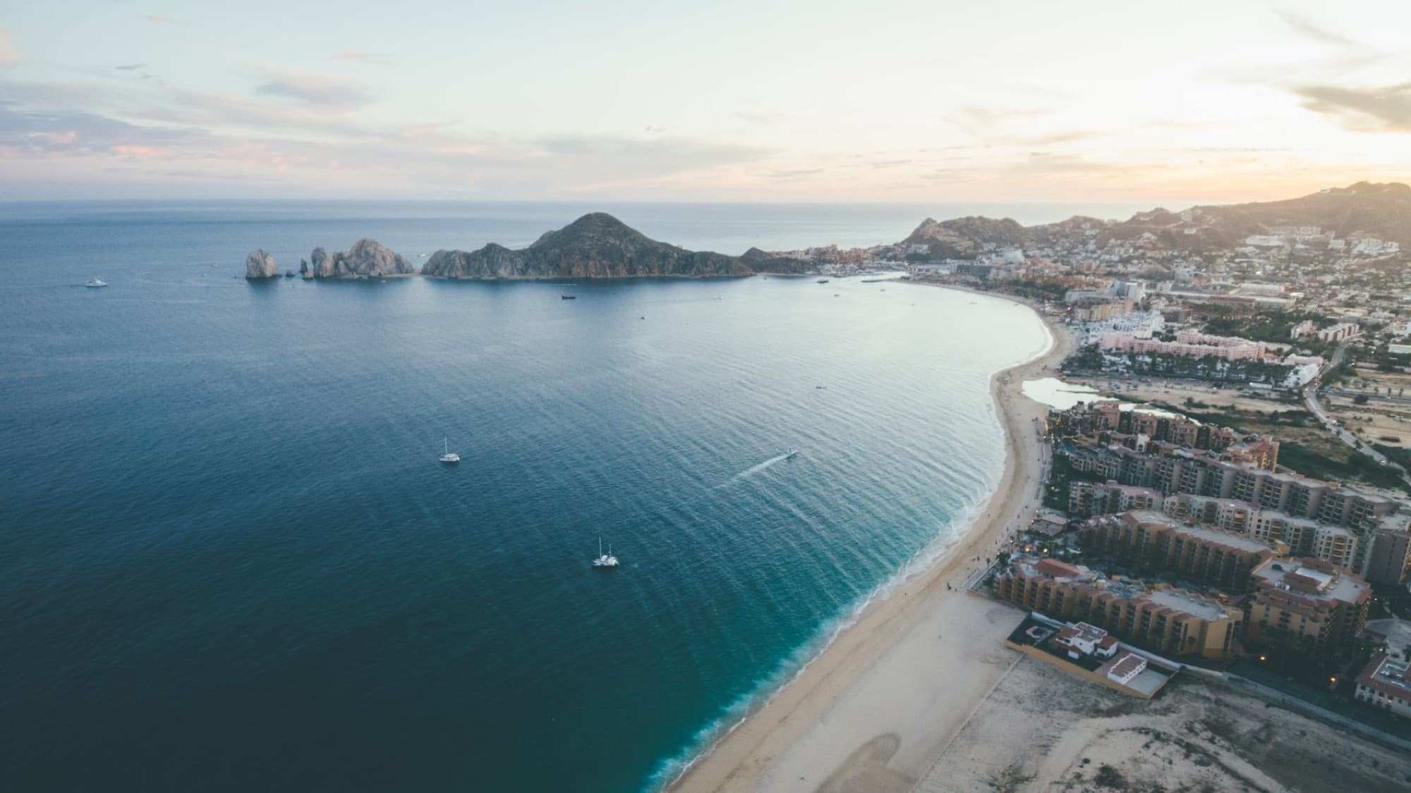 A stunning aerial view of Cabo San Lucas coastline during sunset, showcasing the beautiful seascape and cityscape.