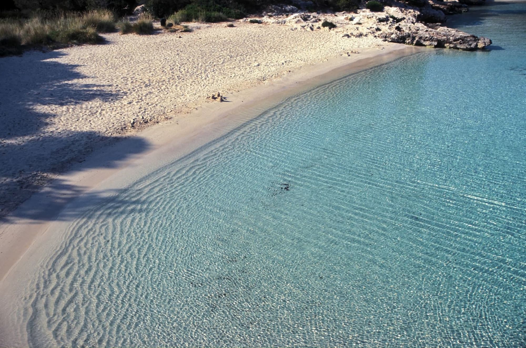 Serene beach in Minorca, Balearic Islands, showcasing clear turquoise waters and soft sand.