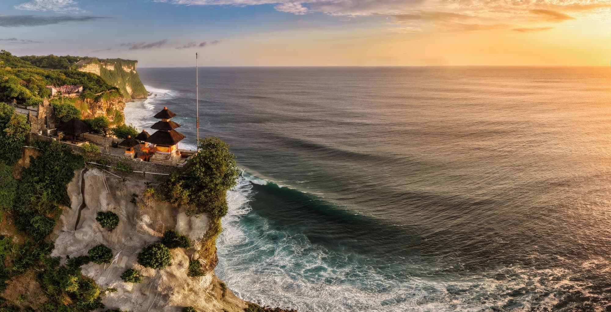 A breathtaking aerial view of Uluwatu Temple perched on cliffs overlooking the ocean at sunset in Bali, Indonesia.
