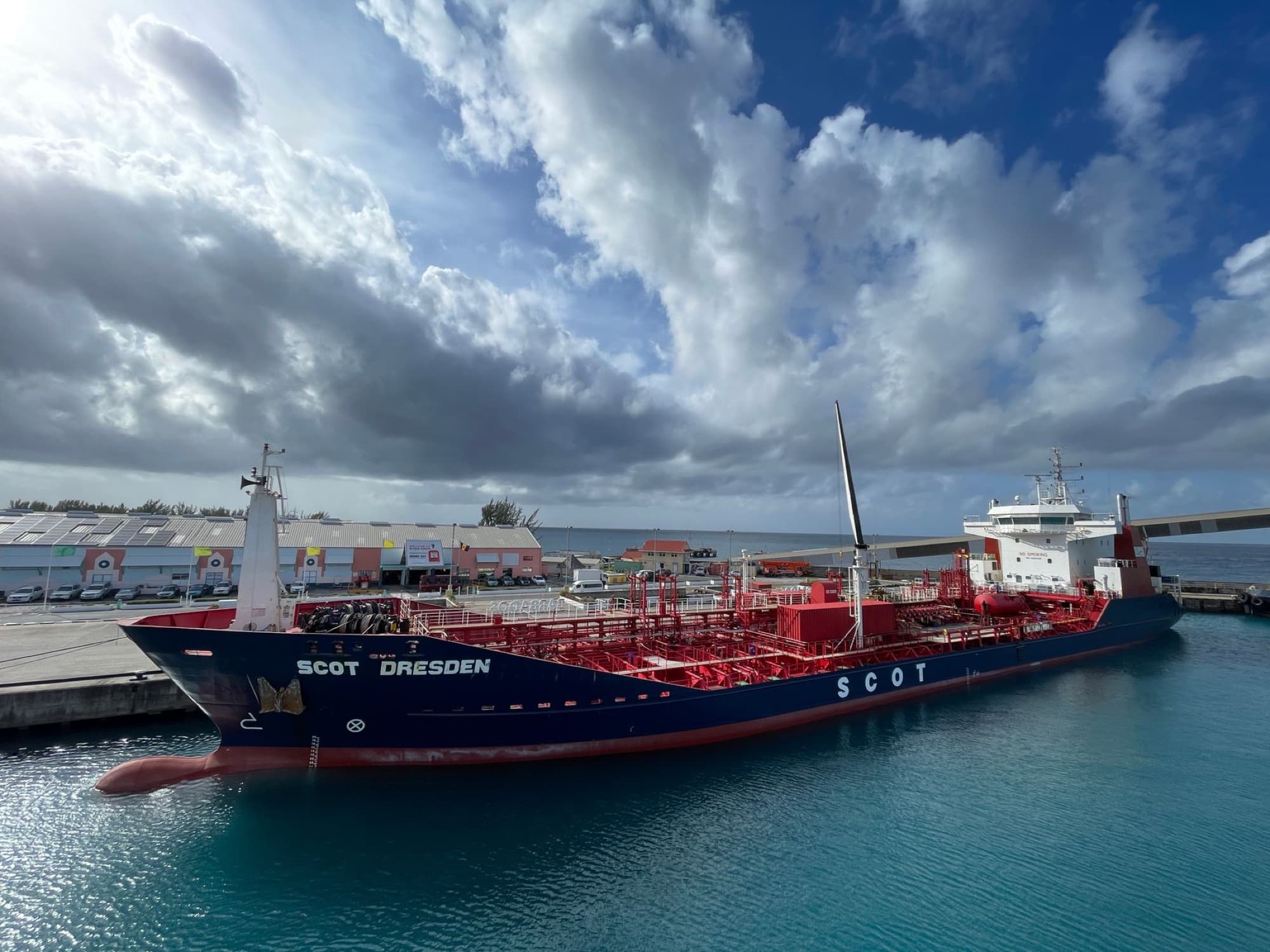 A large container ship docked at a vibrant harbor in Barbados under a partly cloudy sky.