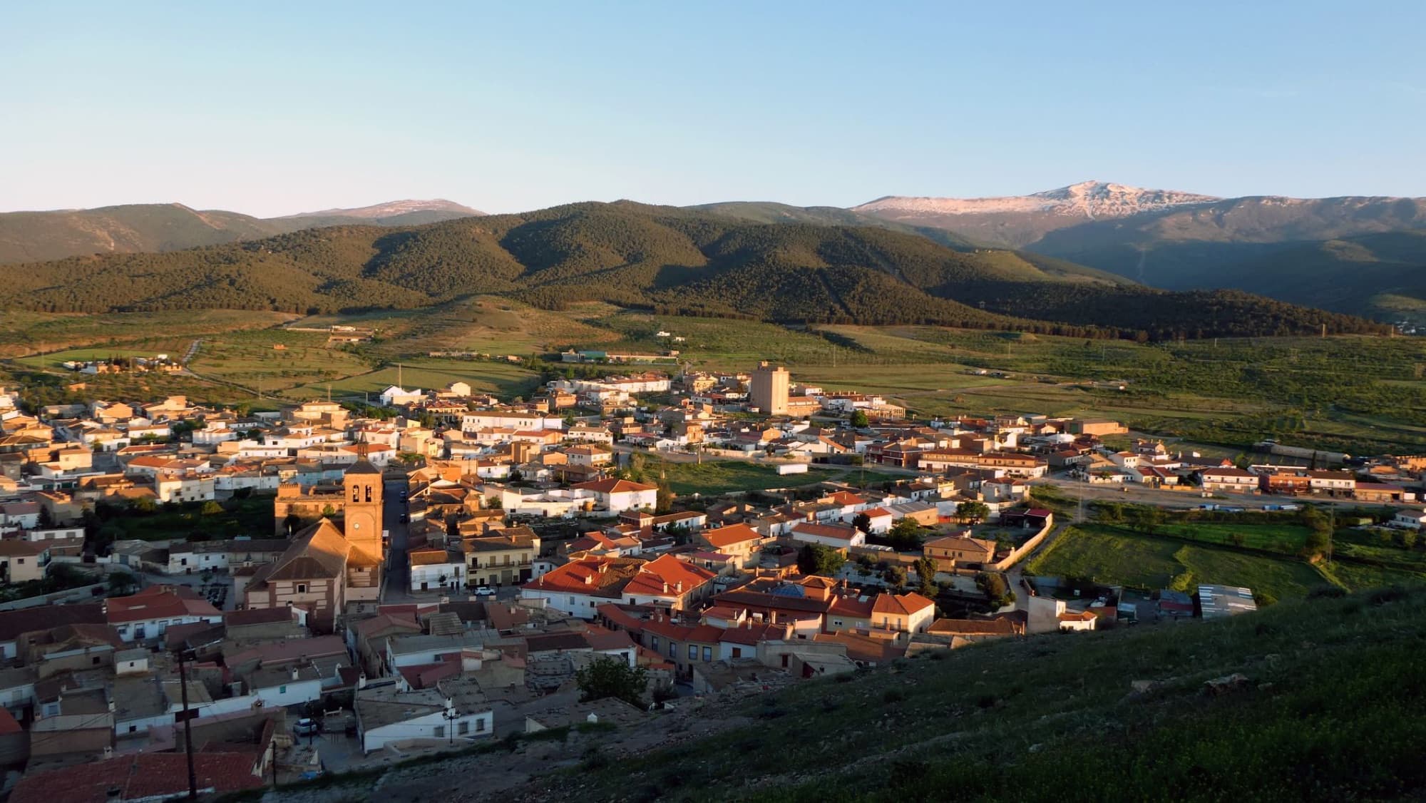 A breathtaking aerial view of a serene village nestled in lush mountains under a clear sky at sunset.