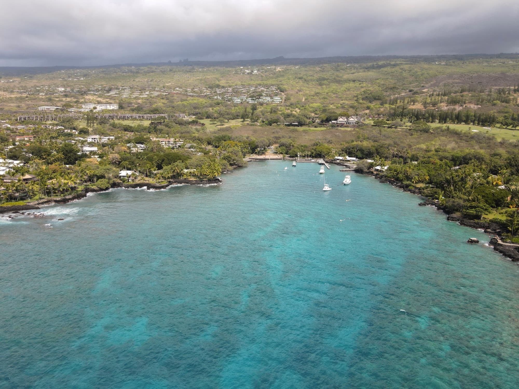 Scenic aerial view of Kailua-Kona, Hawaii coastline featuring boats and lush greenery.