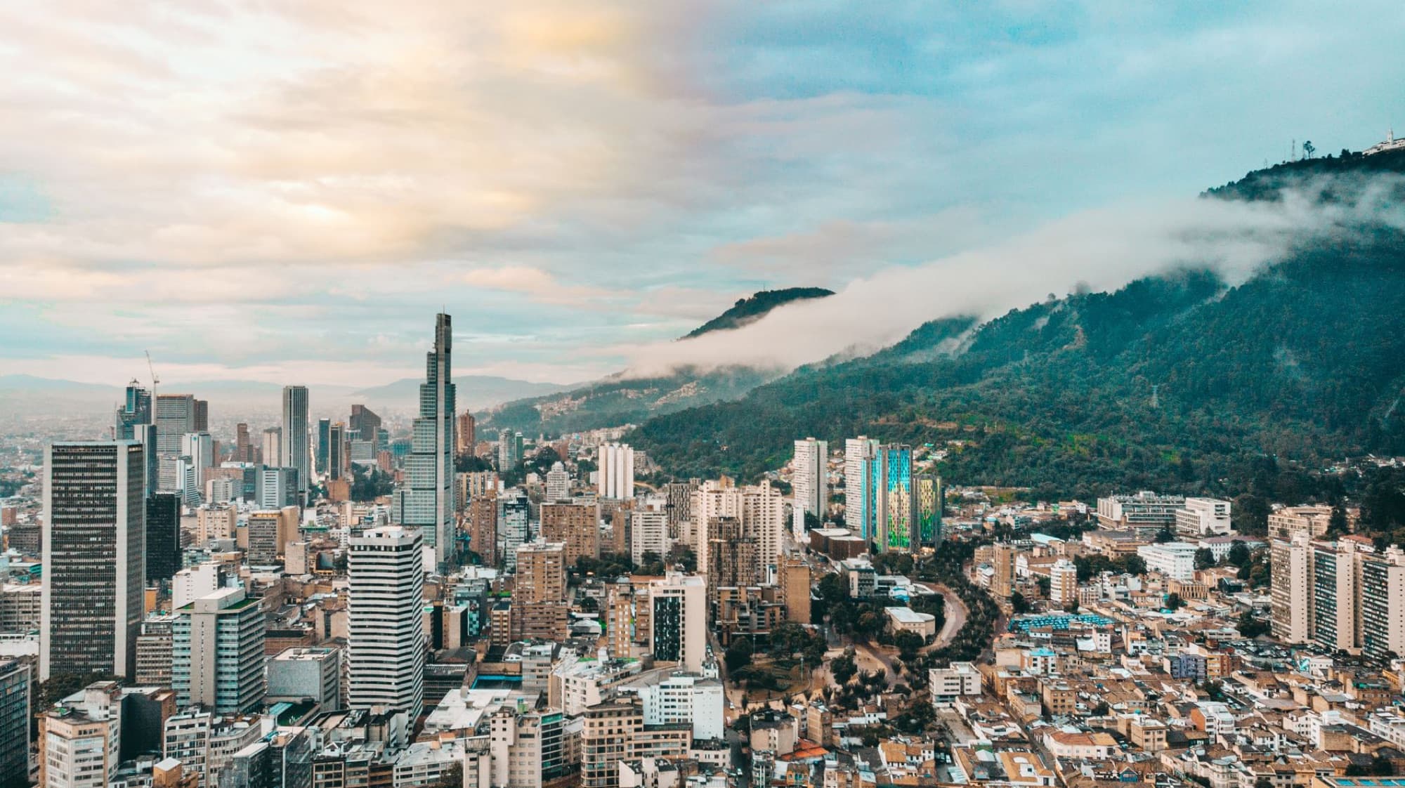 Dramatic aerial shot of Bogotá's skyline with mountain backdrop and clouds.
