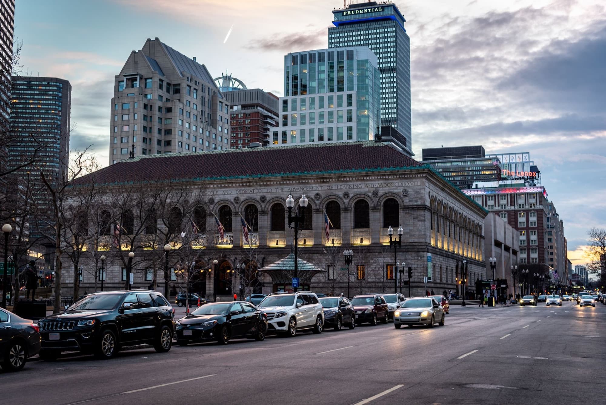 A street view of Boston Public Library and skyline at dusk, capturing urban architecture and city life.