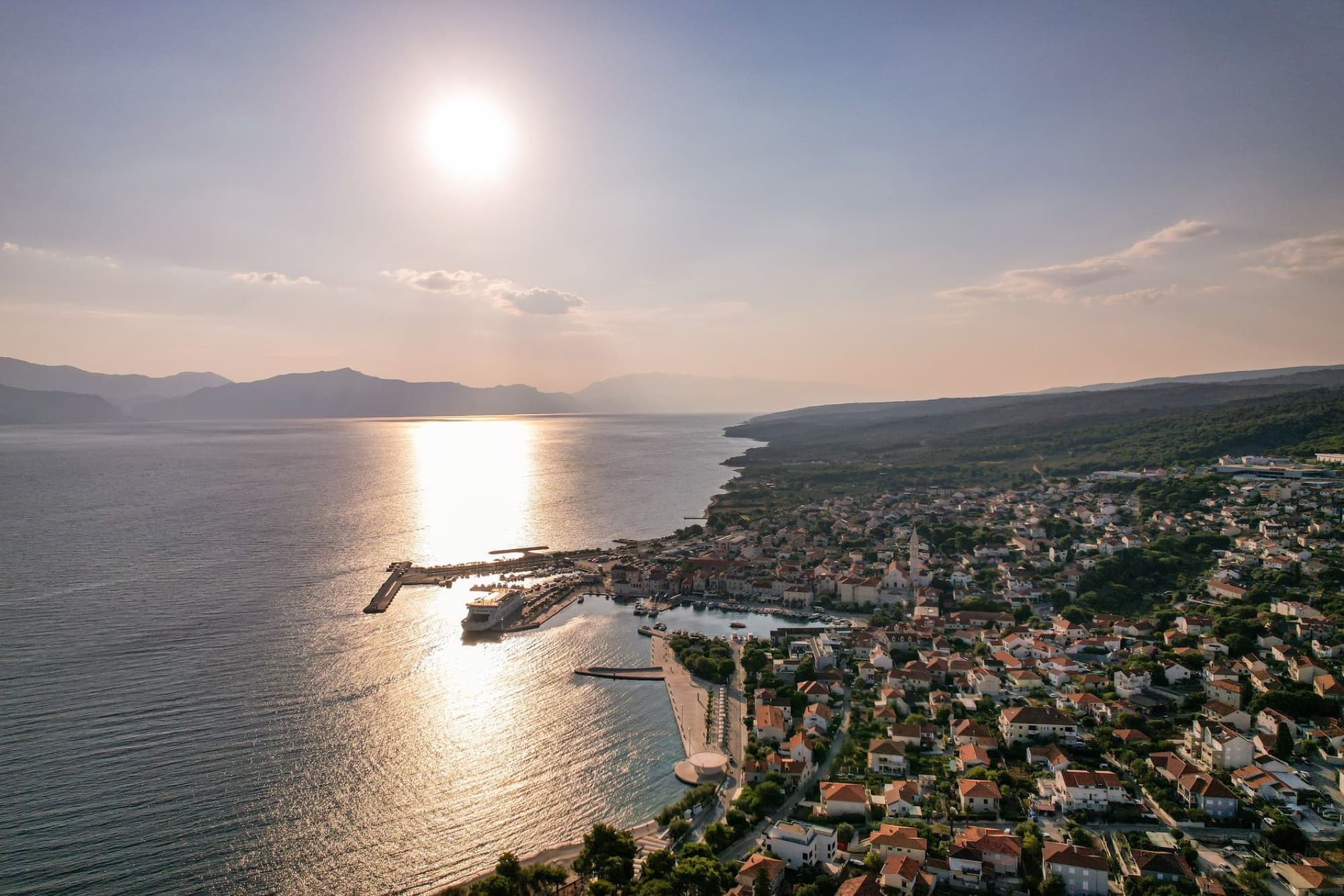 Scenic aerial shot of a coastal town under the setting sun with mountains in the background.