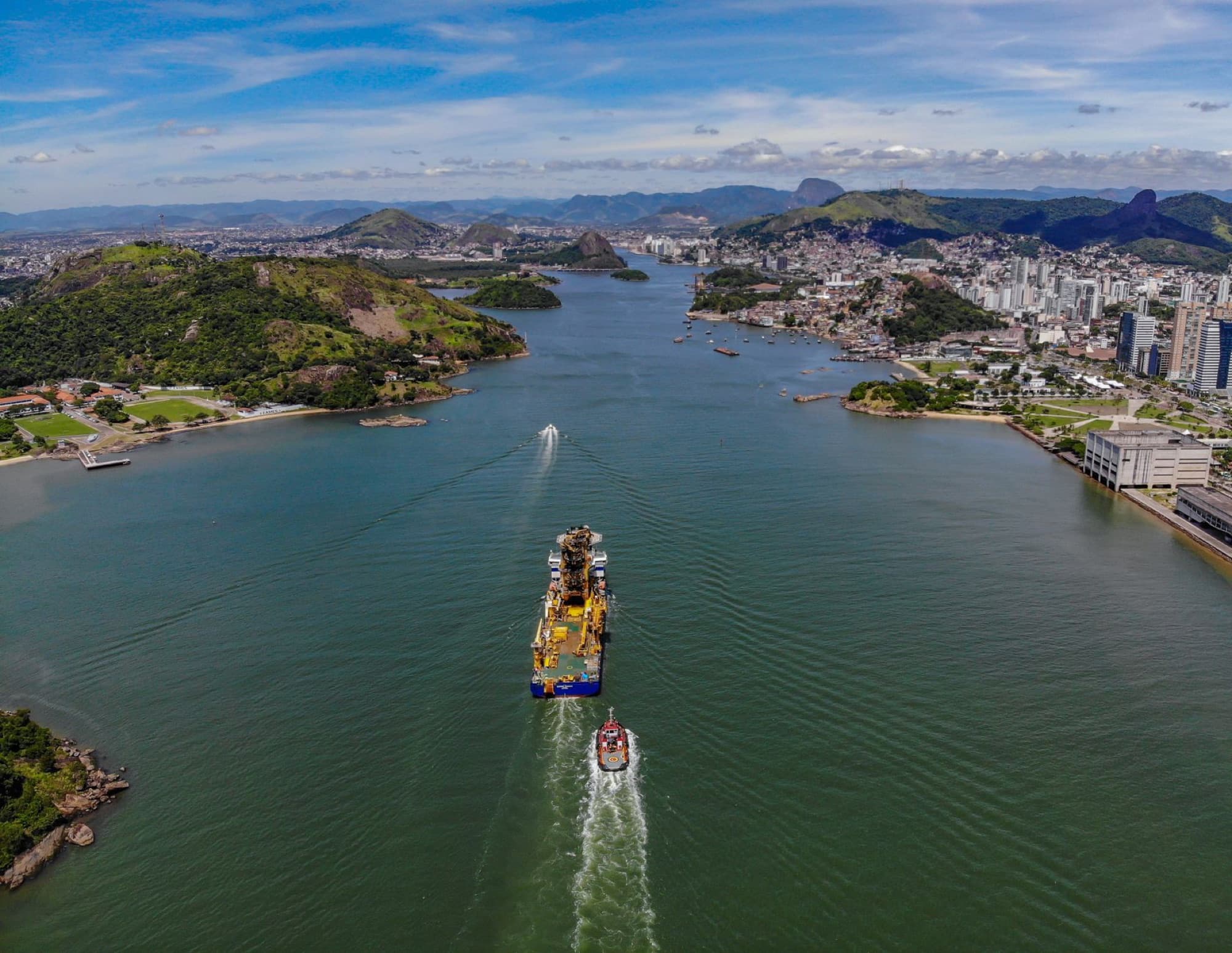 Aerial view of Vitória, Brazil, showcasing the city's waterfront and a large ship navigating the channel.