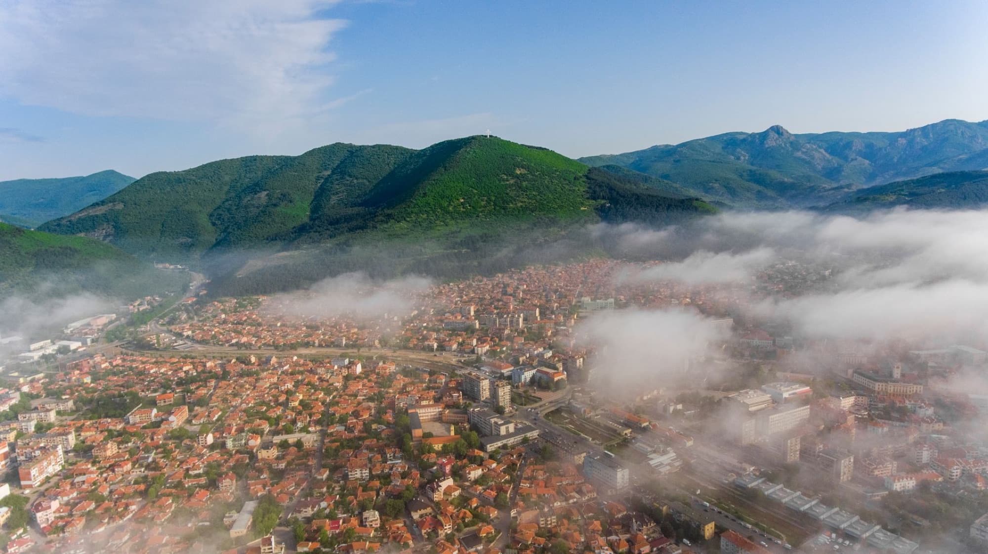 Scenic aerial view of a Bulgarian town surrounded by mist and lush green mountains.