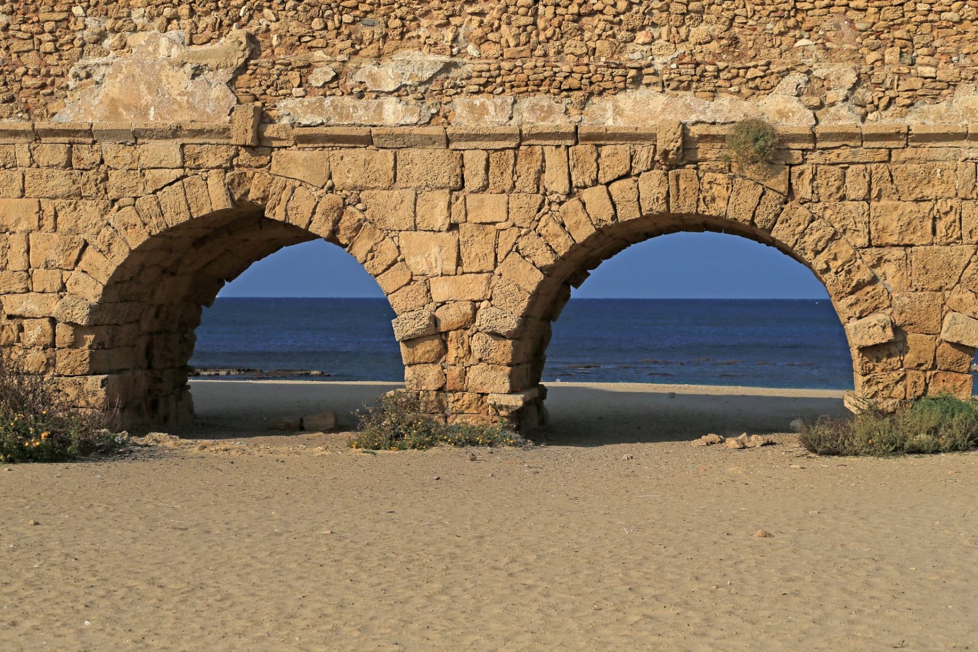 View of the ancient Roman aqueduct on the beach at Caesarea, Israel, with the sea in the background.