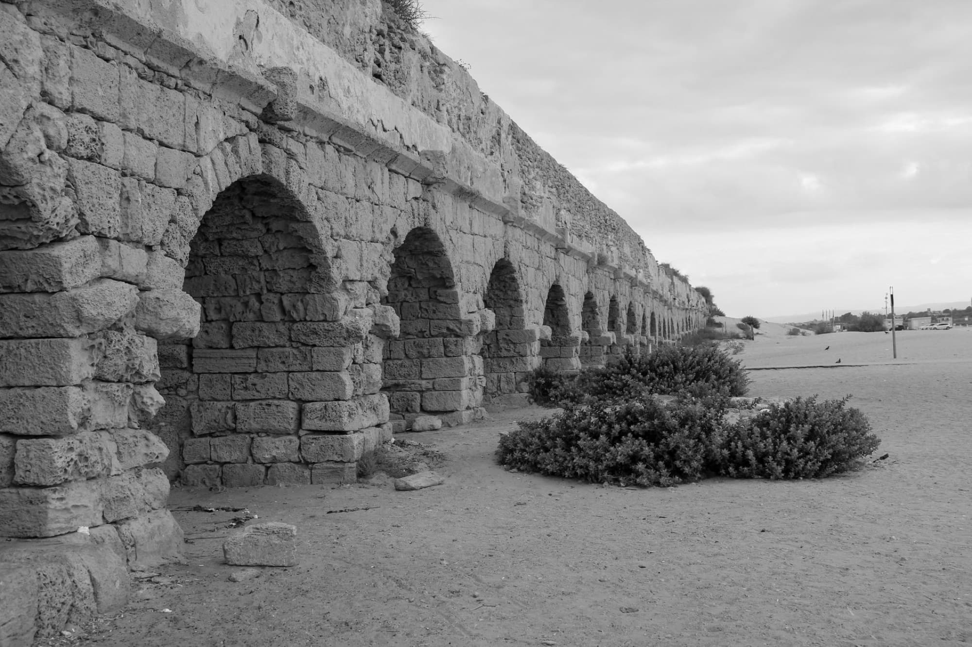 Black and white image of ancient Roman aqueduct arches on a sandy beach in Caesarea, Israel.