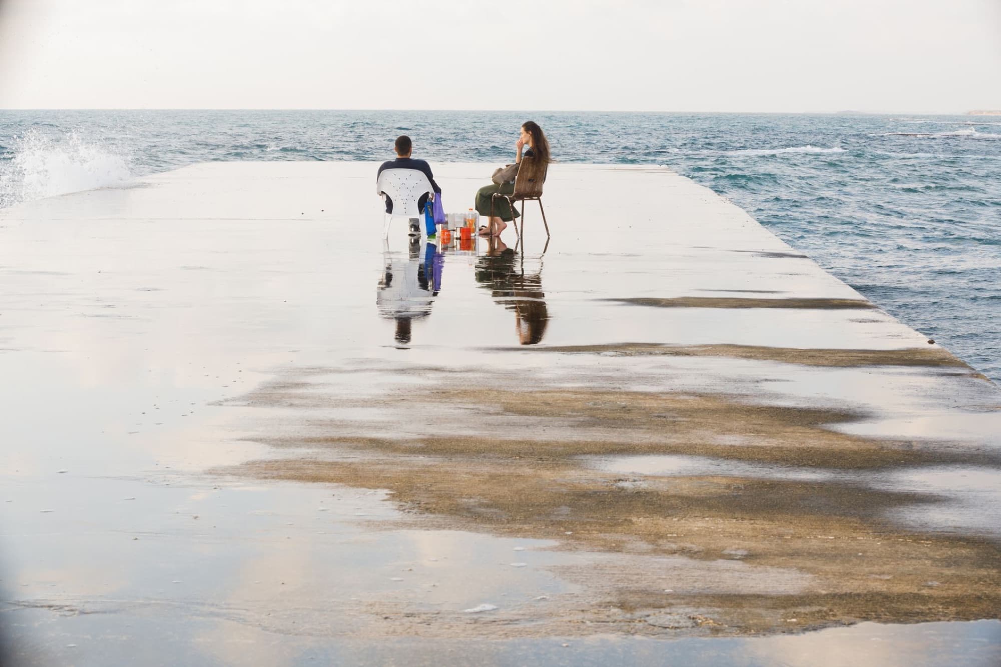 A couple enjoying a calm day by the seaside on a sunlit dock in Caesarea, Israel.