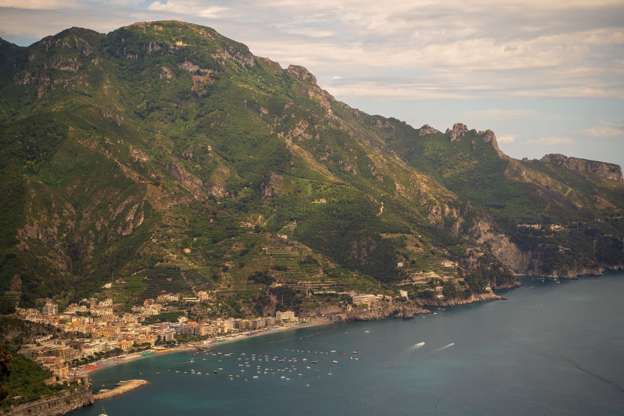 A scenic aerial view of a coastal town nestled beside dramatic green mountains.