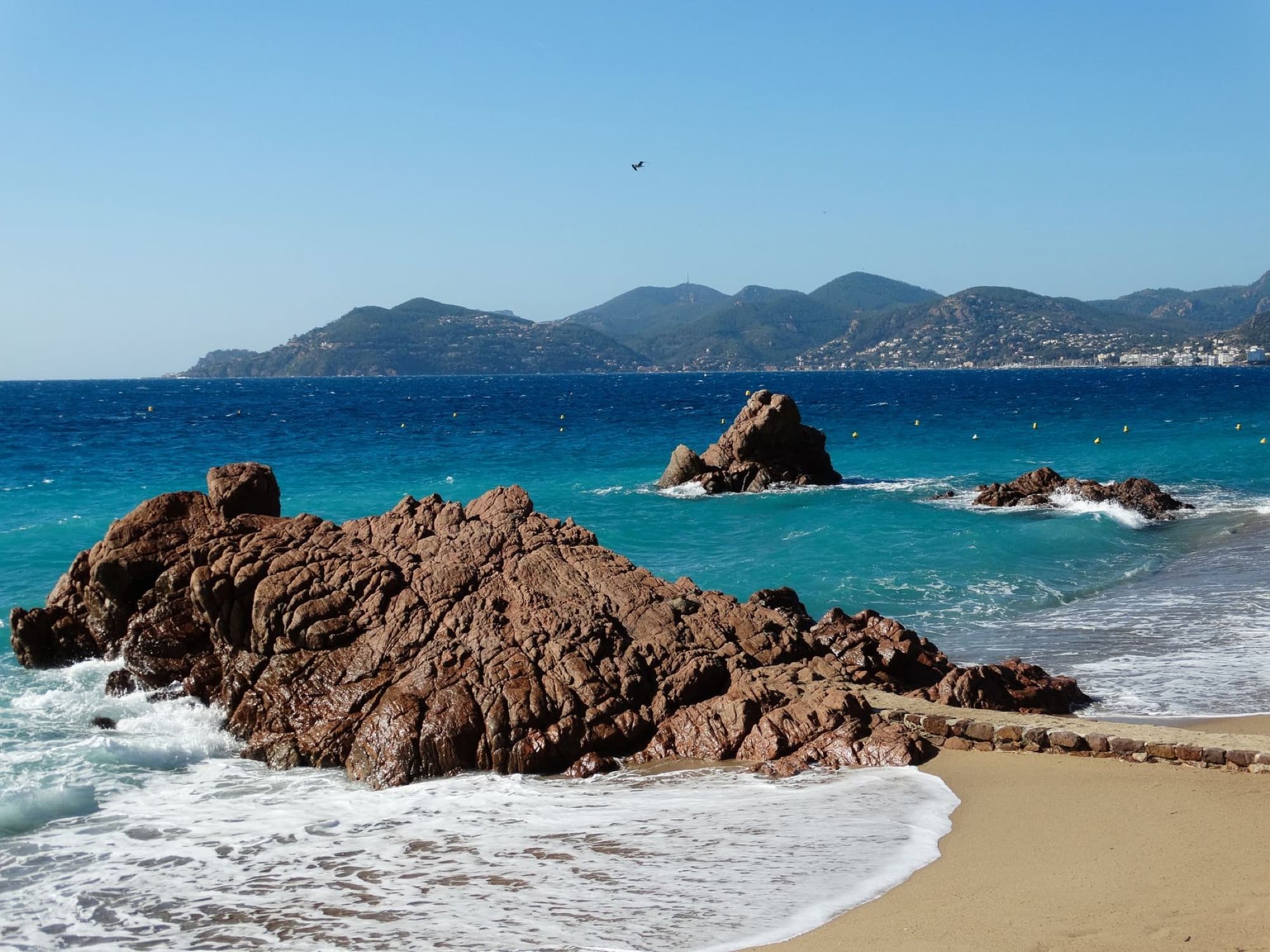 Stunning rocky shoreline in Cannes, Provence-Alpes-Côte d'Azur, France, featuring azure waters and distant mountains.