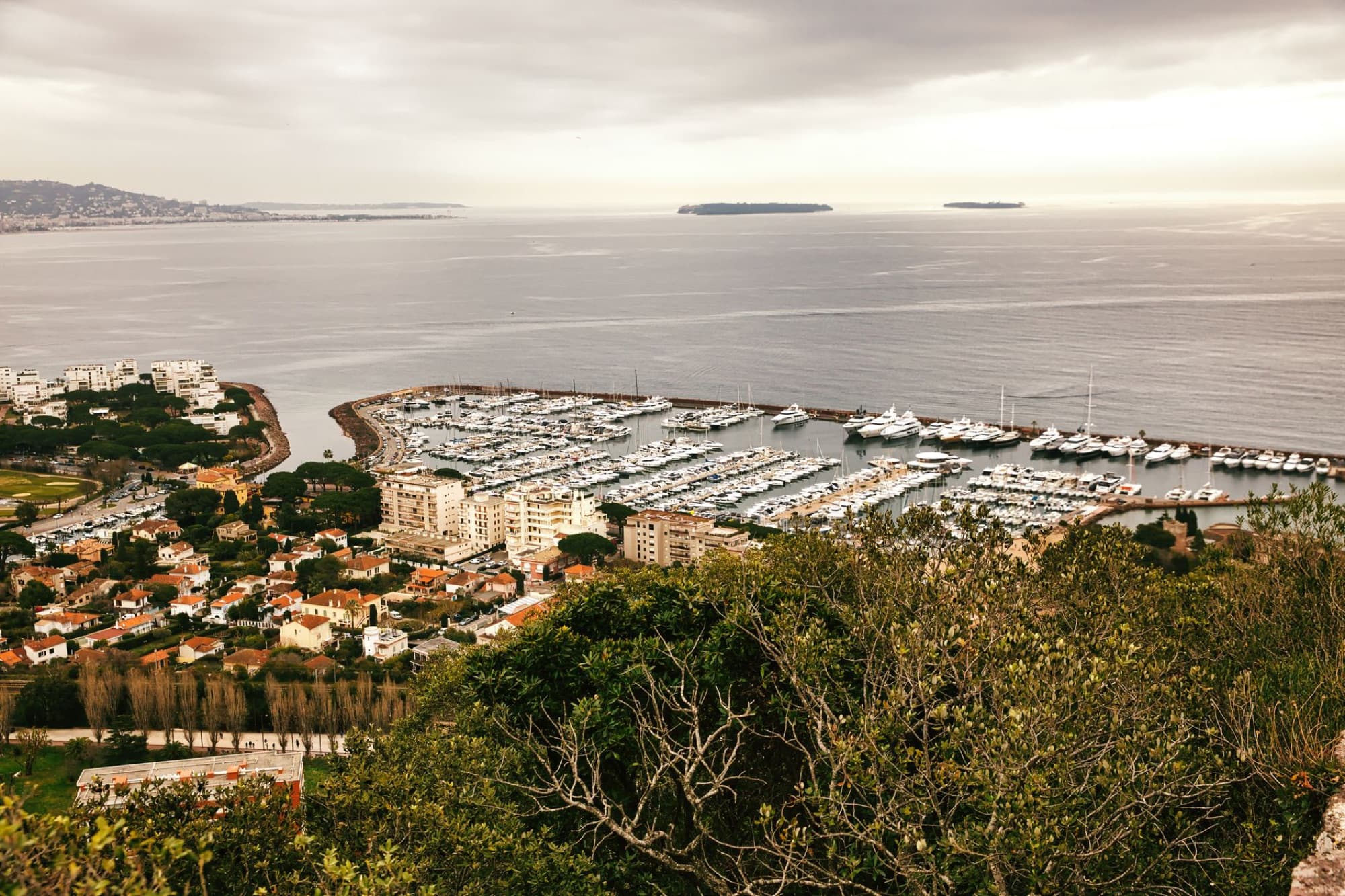 Stunning aerial view of the Cannes Marina and coastal landscape on a cloudy day, highlighting the serene bay area.