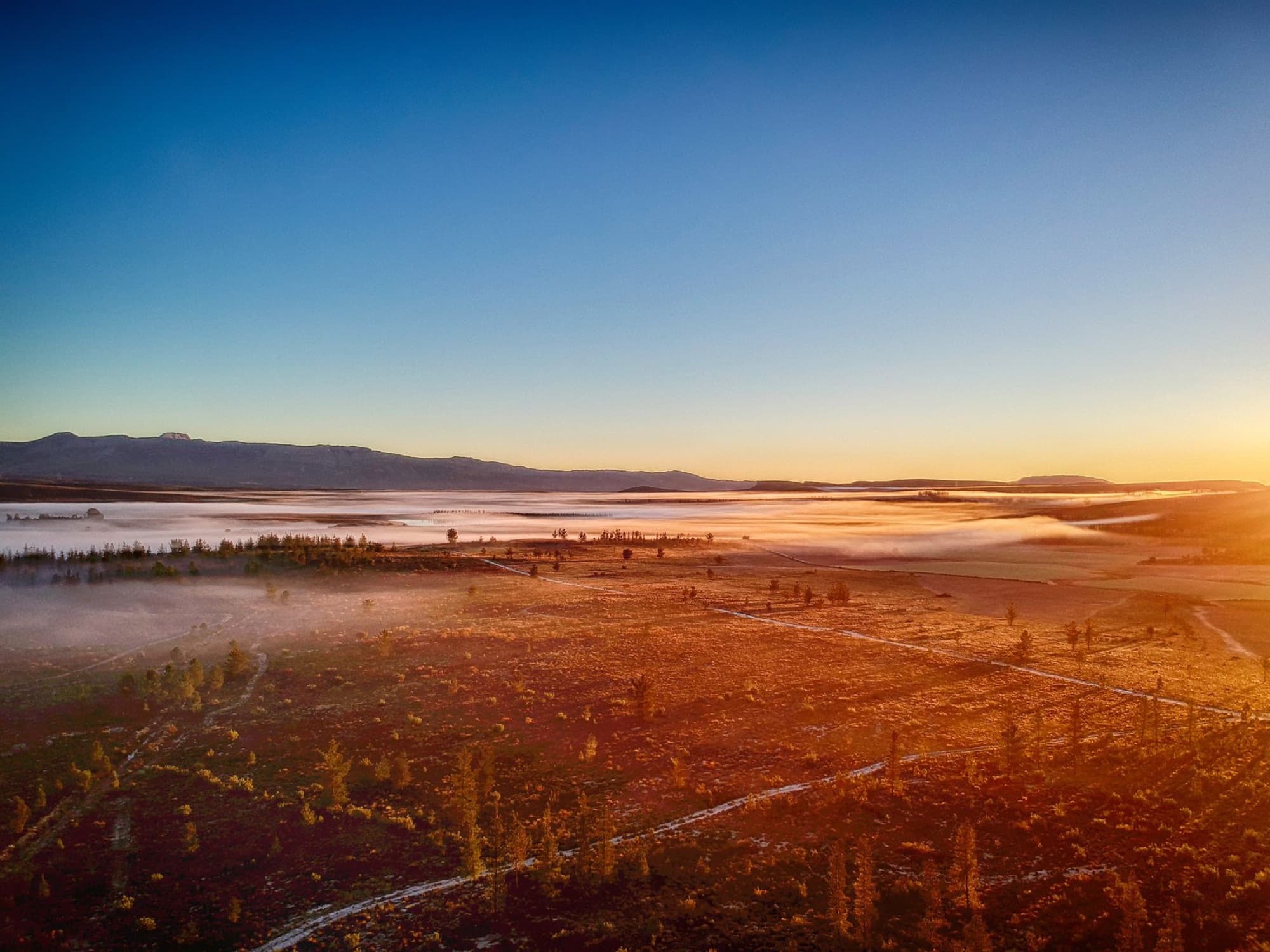 A breathtaking aerial view of the Matroosberg mountains at sunrise, capturing a serene landscape shrouded in morning fog.