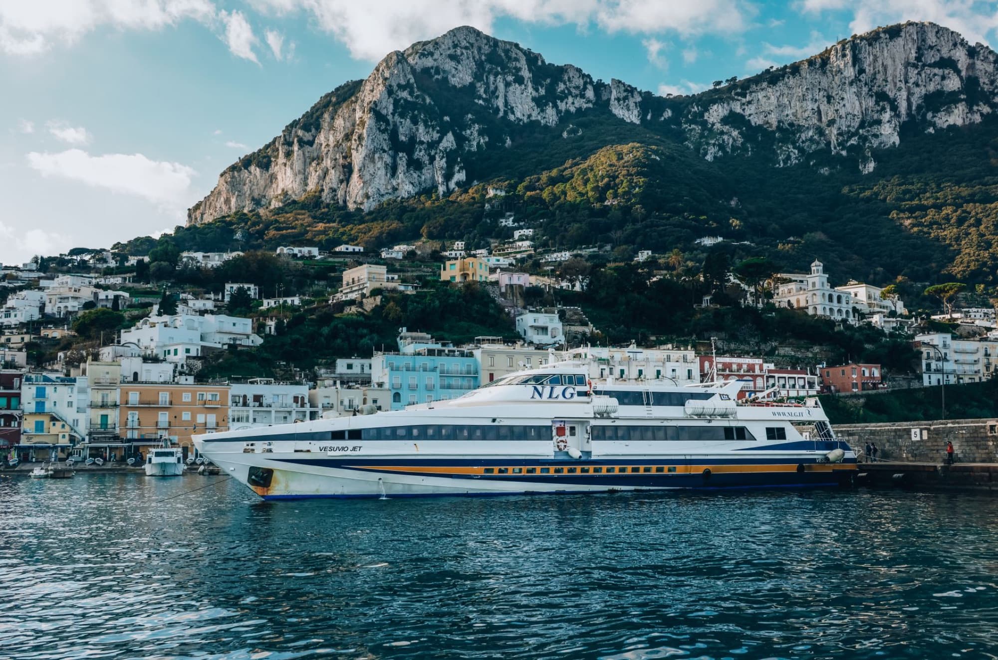 A ferry docked at Capri Island harbor with stunning mountain and town view.