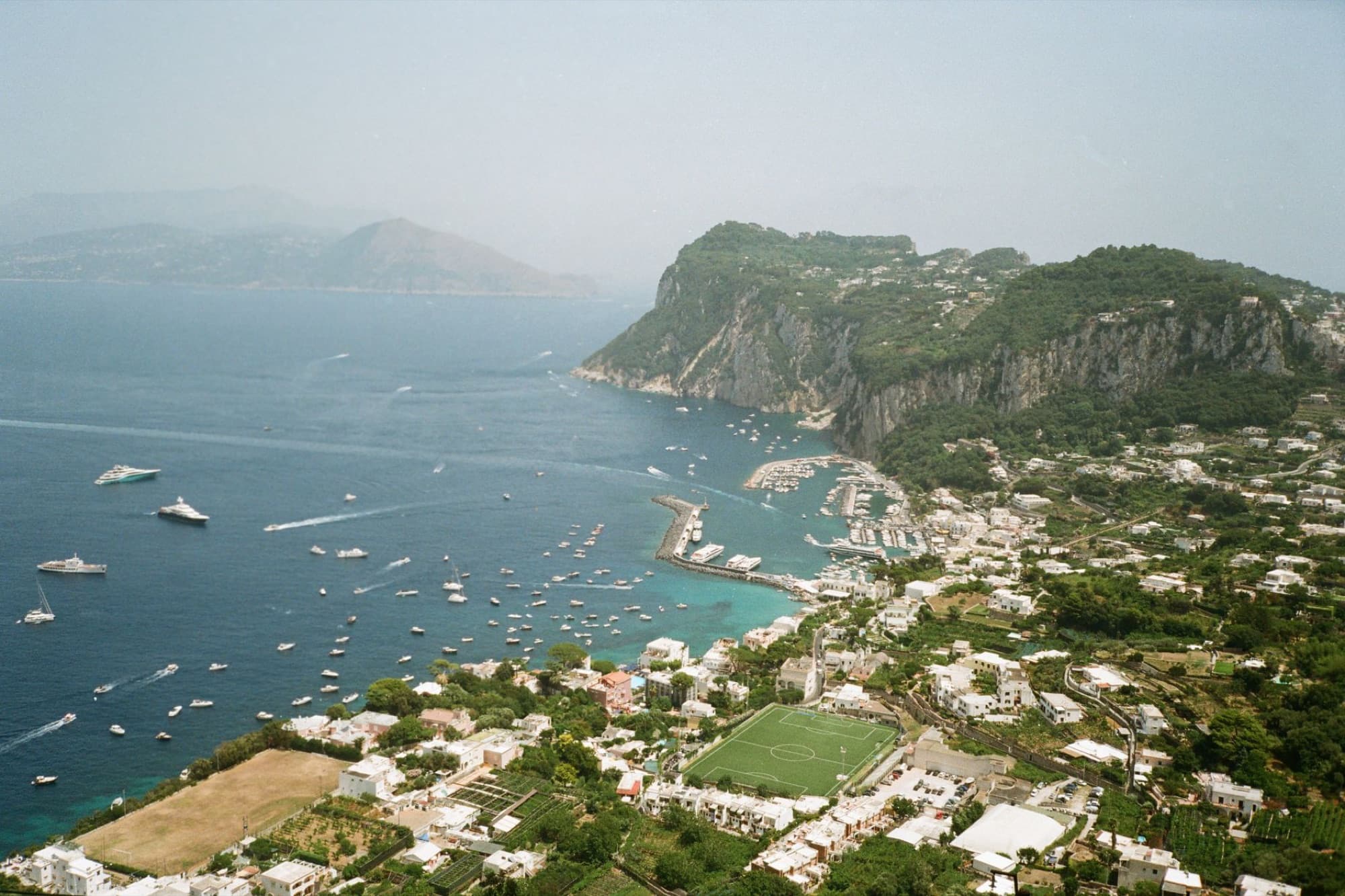 Stunning aerial view of Capri's coastline with boats and lush hills, overlooking the marina and harbor.