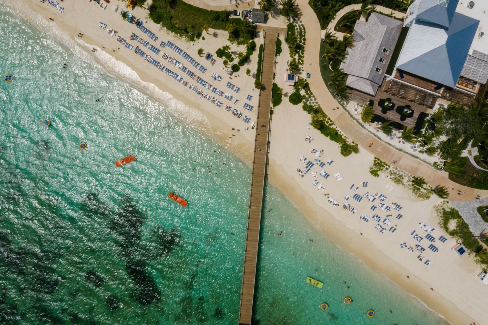 Stunning aerial shot of a sandy beach with clear turquoise waters and a wooden pier.