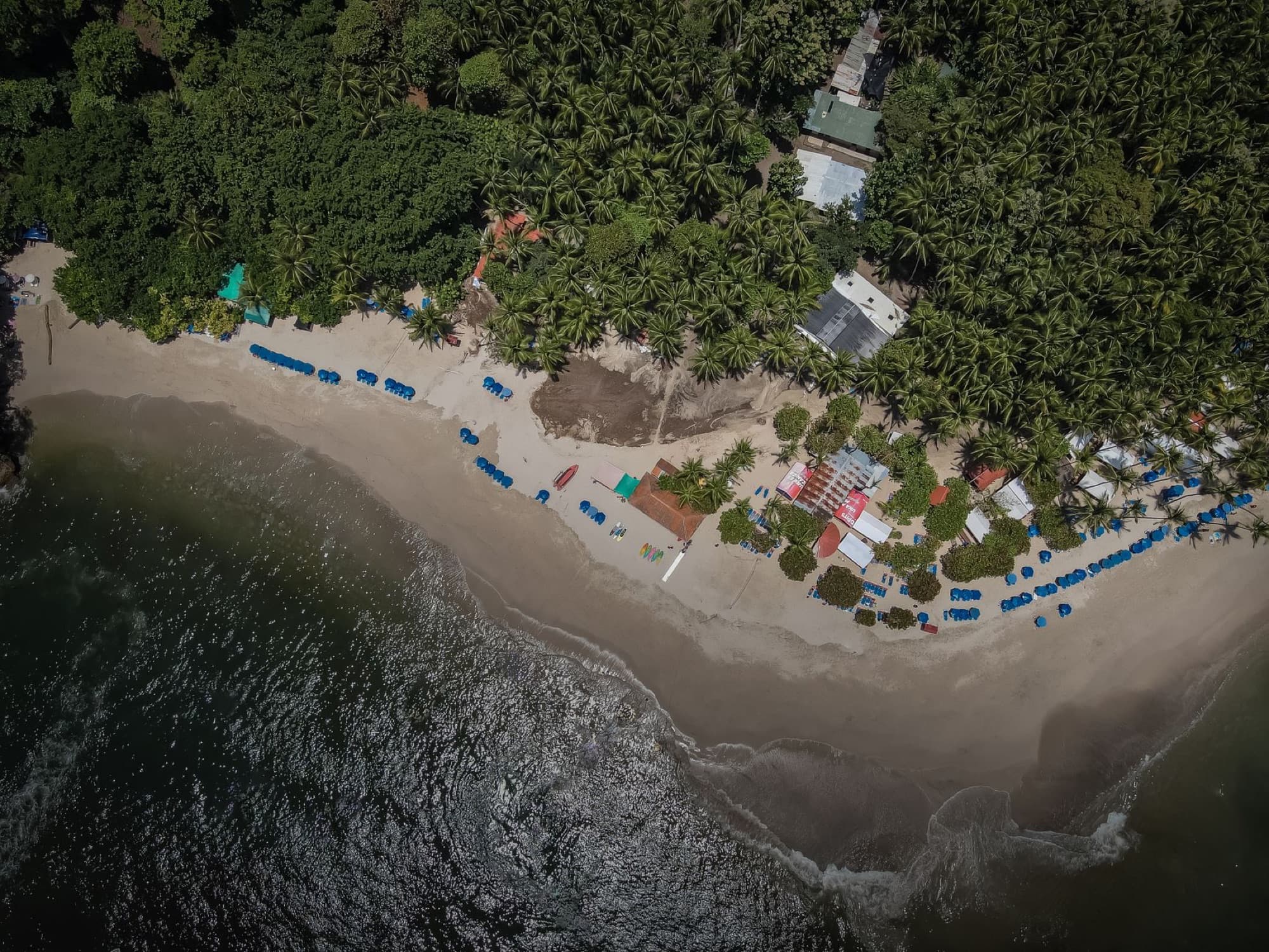 Drone shot of a picturesque beach in Paquera, Costa Rica, surrounded by lush palms.