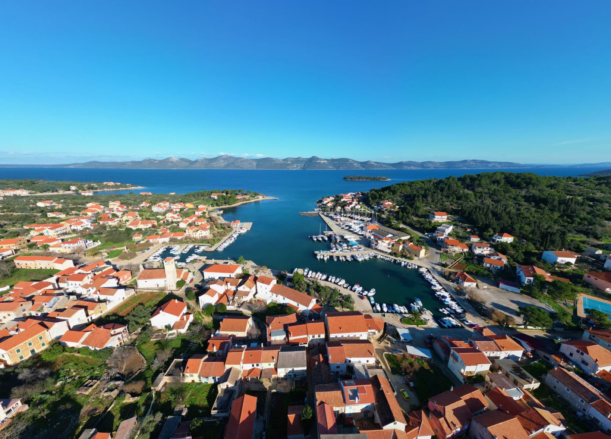 Scenic aerial view of Veli Iž harbor with red-roofed houses and clear blue sea in Croatia.