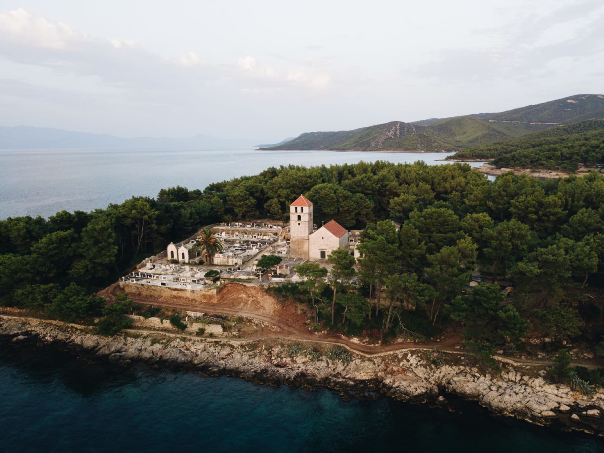 A serene aerial view of a historic church nestled amid lush greenery along the scenic Jelsa coastline in Croatia.
