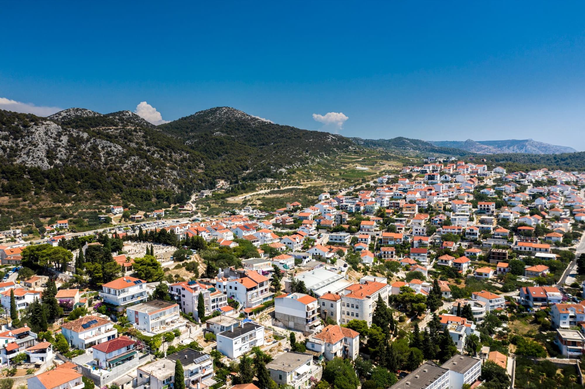 A stunning aerial view of a Croatian town with red-roofed houses surrounded by lush hills under a clear blue sky.