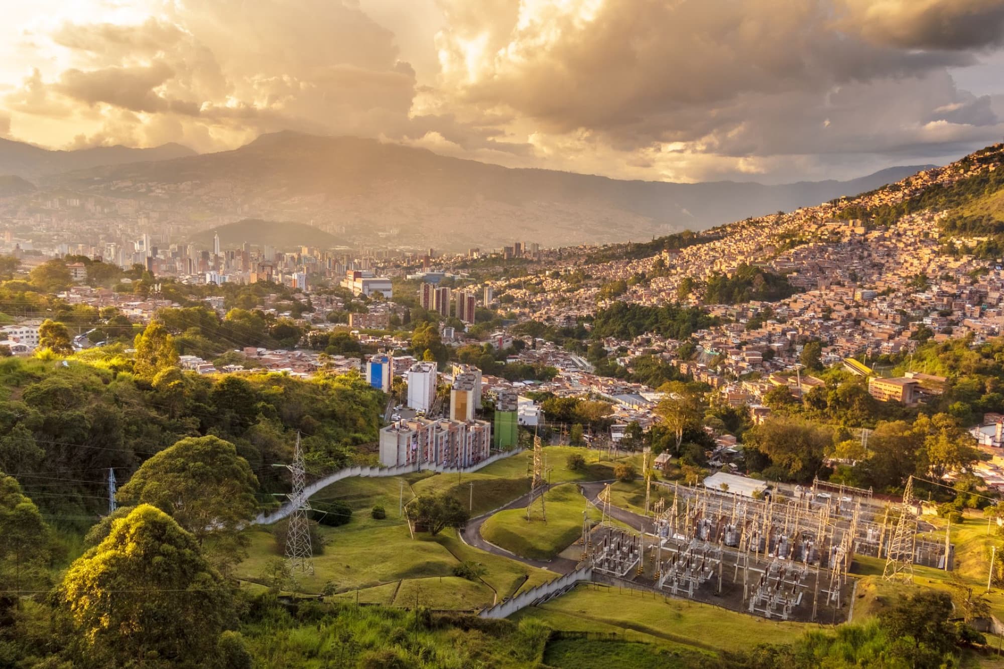 Aerial shot of Medellin, Colombia, showcasing urban sprawl and hills at sunset.