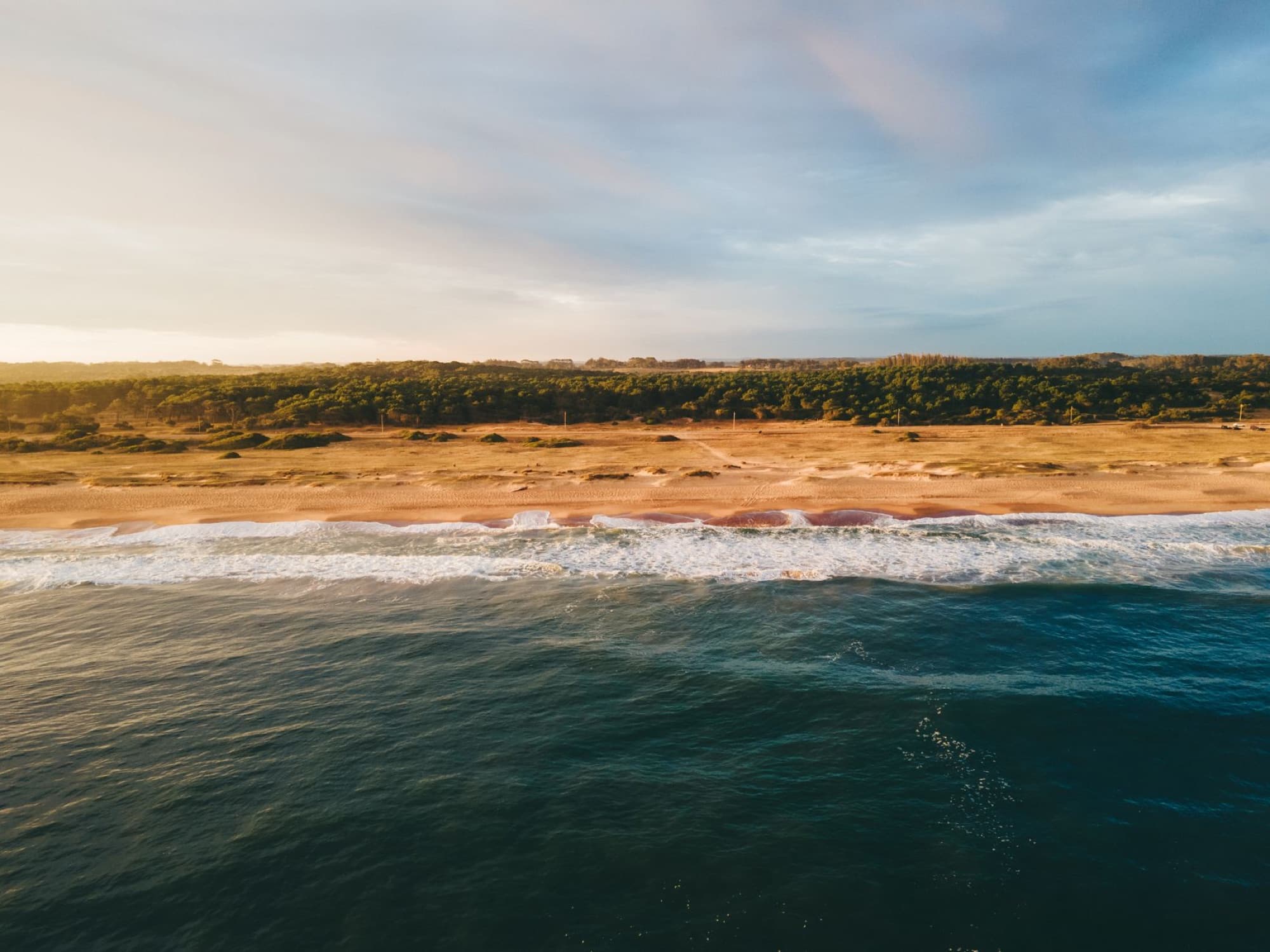 Captivating aerial view of a pristine beach shoreline in Garzón, Uruguay at sunset, showcasing nature's beauty.