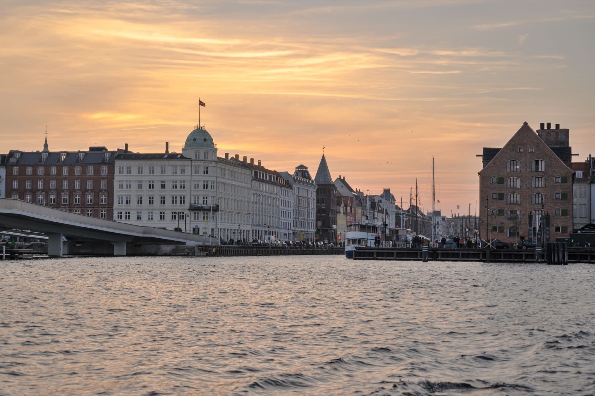 Scenic view of Copenhagen's waterfront during sunset with historic buildings and calm river.