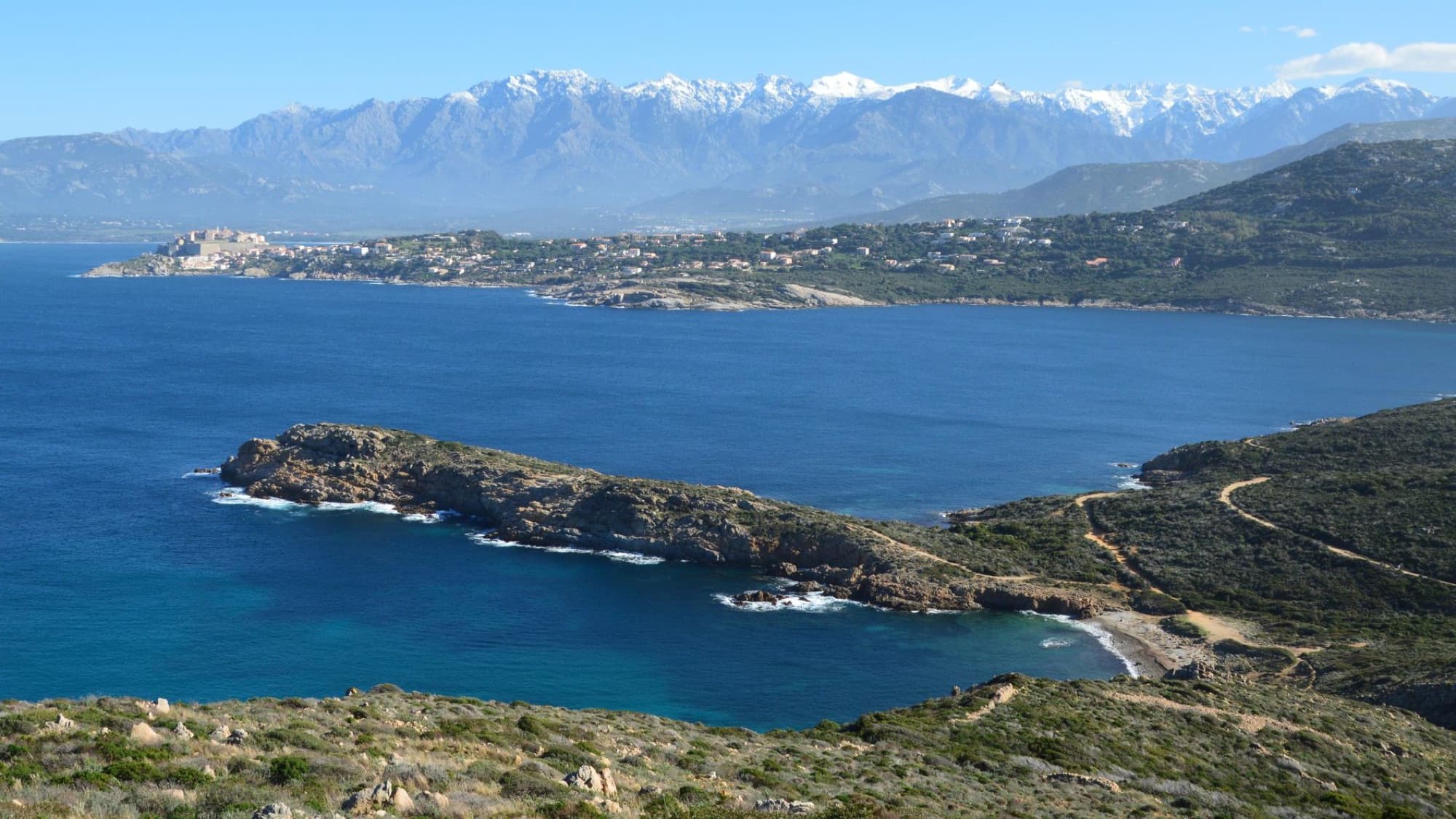 Breathtaking aerial view of the picturesque coastline of Calvi, Corsica with mountains in the background.