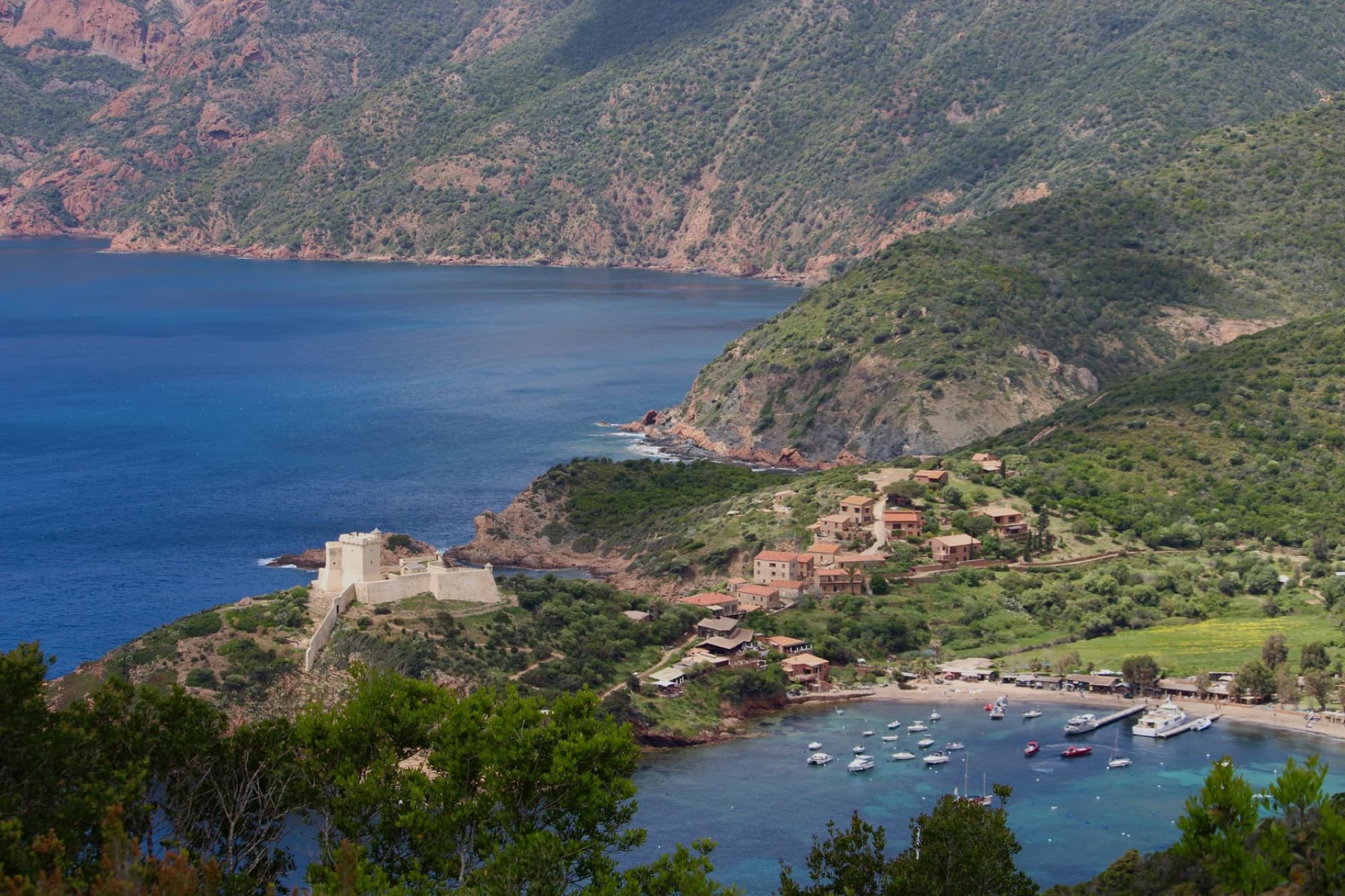 Explore the scenic coastline of Corsica with a historic castle and vibrant turquoise sea.