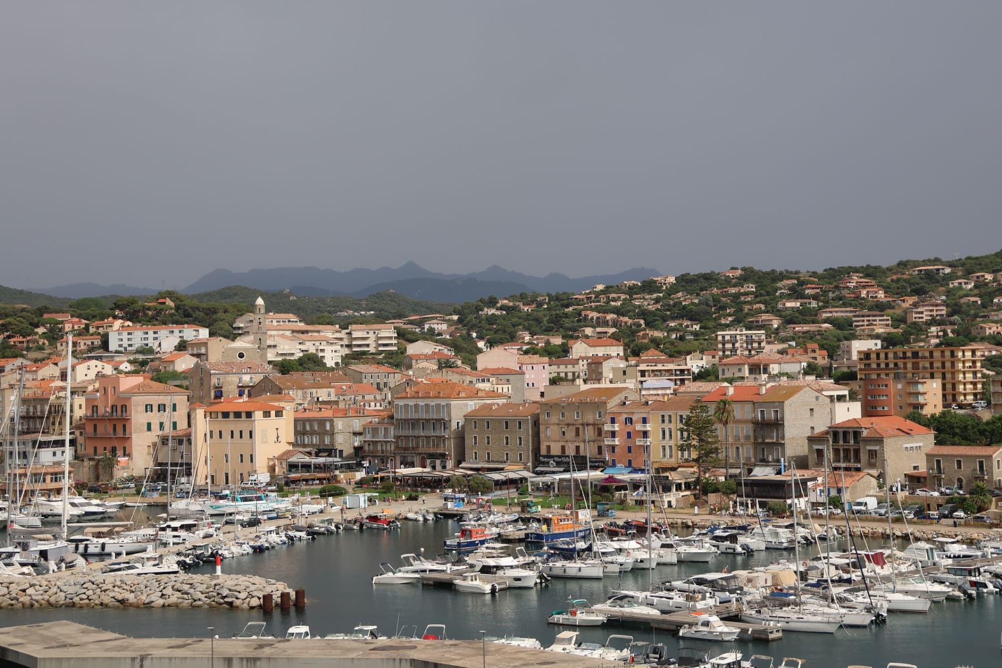 Beautiful view of Propriano harbor with boats and historic buildings, set against hilly landscape in Corsica.