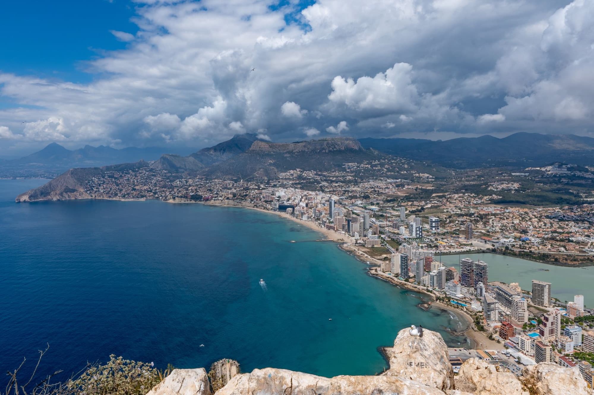 Scenic aerial view of Calpe's coastline and urban skyline under clouded skies.