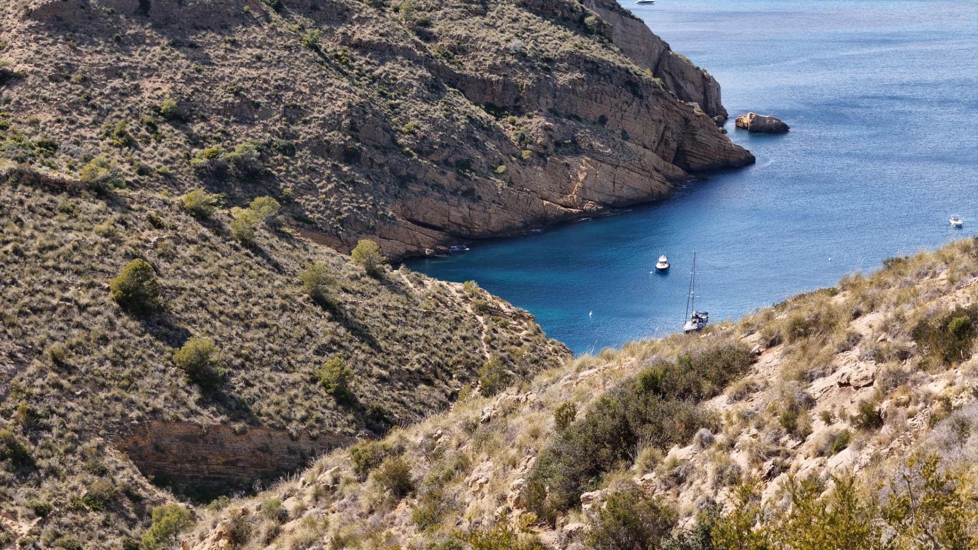 Aerial view of a picturesque cove with boats surrounded by rugged cliffs in the Mediterranean coast of Spain.