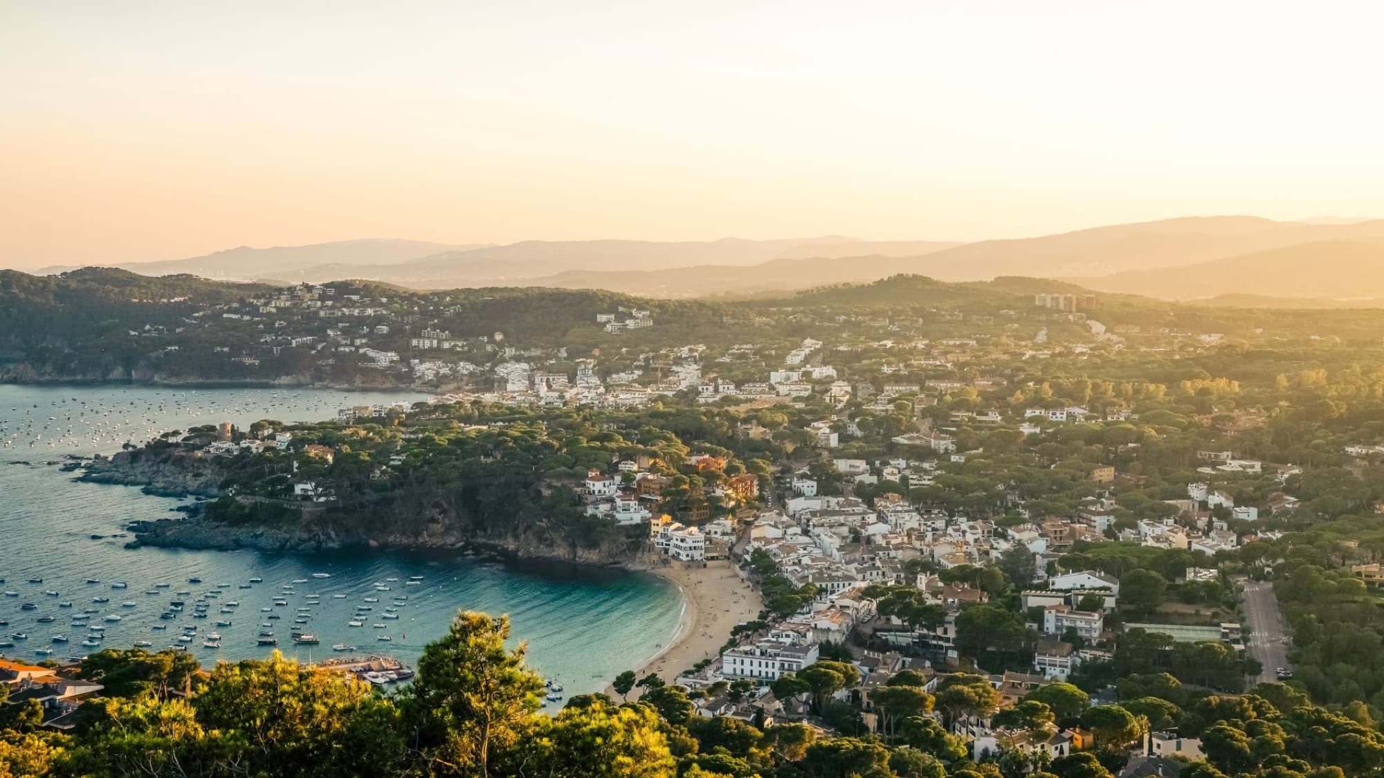 A mesmerizing aerial view of Llafranc, Spain, showcasing the coastline, beach, and cove during sunset.