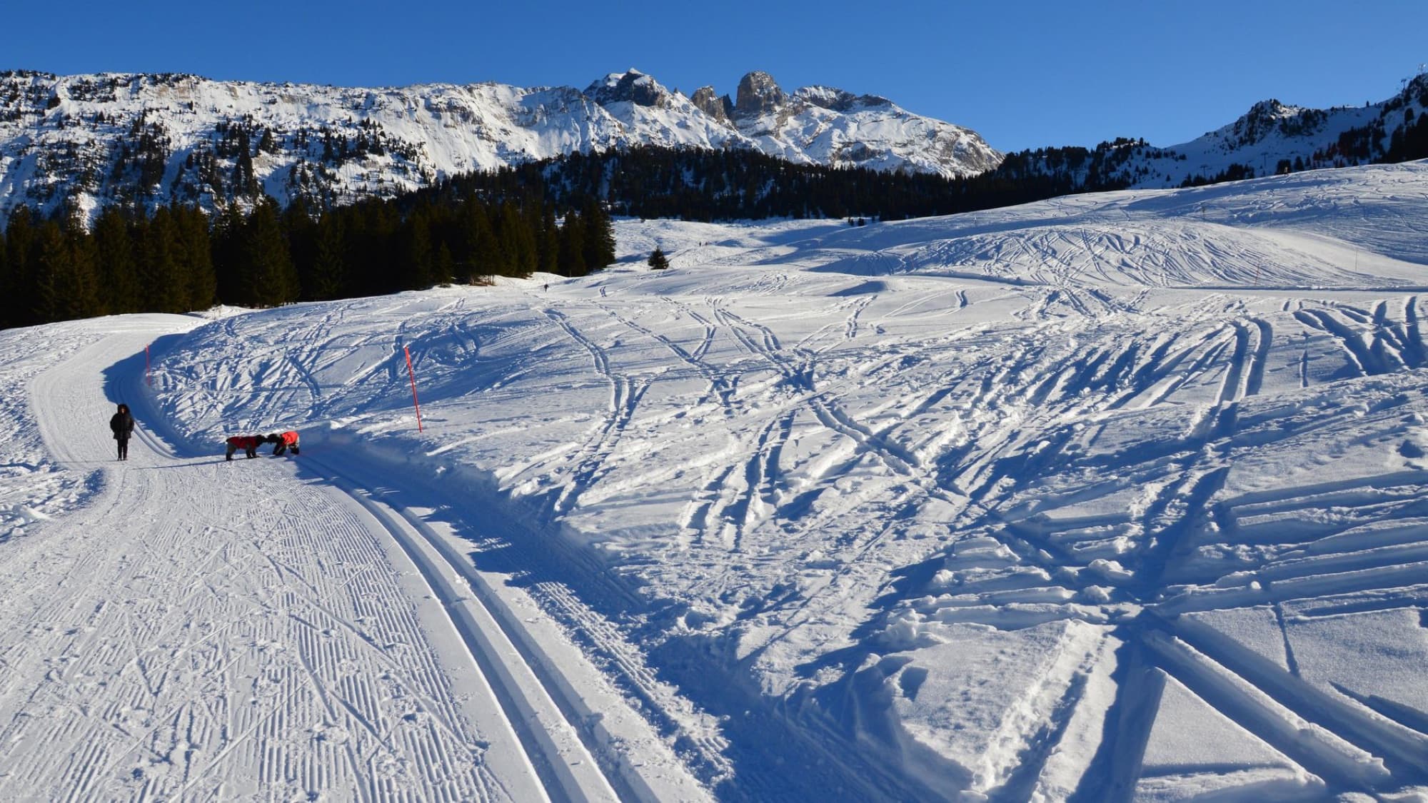 A winter trail in Courchevel with snow-covered mountains under a clear blue sky.