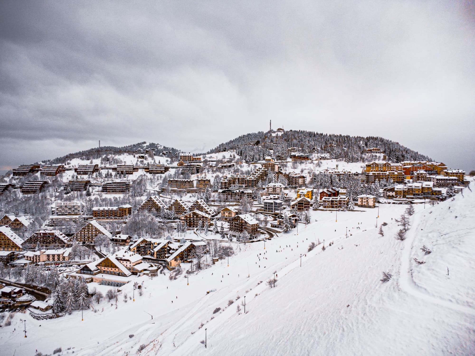 Aerial view of a snow-covered mountain village featuring ski slopes and scenic winter landscapes.