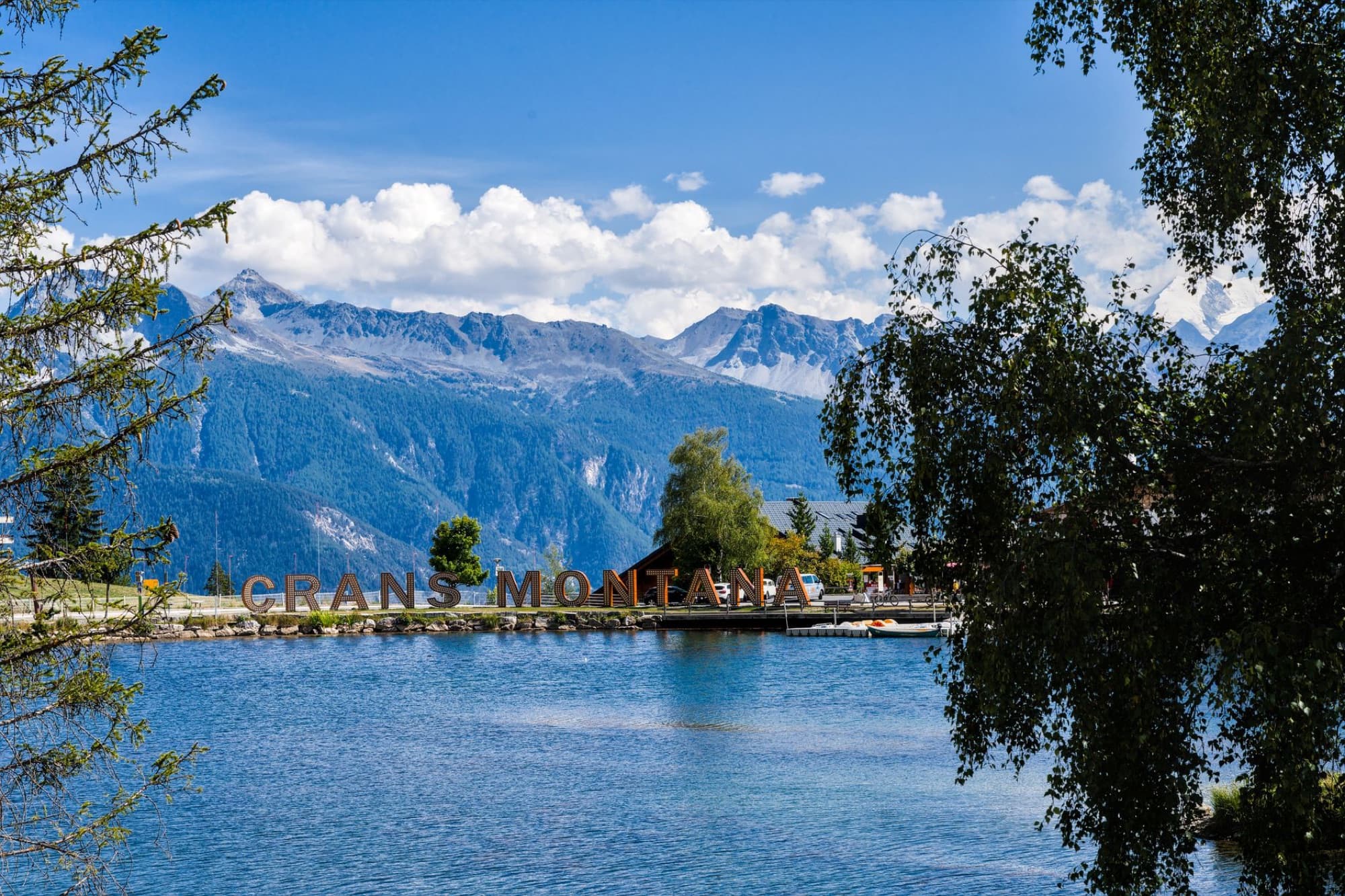 Serene landscape of Crans-Montana with lake, trees, and distant mountains in Switzerland.