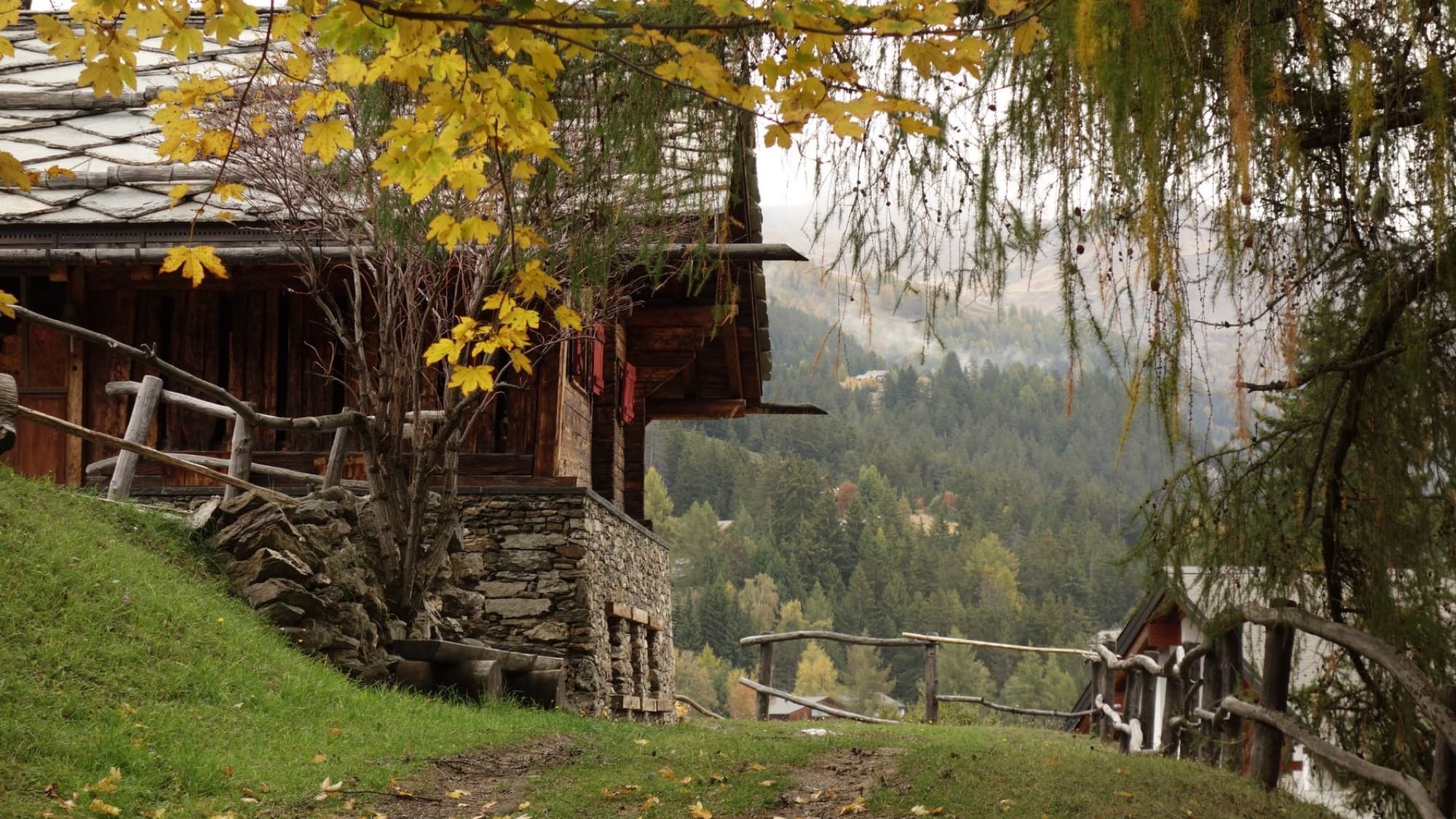 Rustic cabin in Crans-Montana surrounded by autumn foliage and scenic mountains.