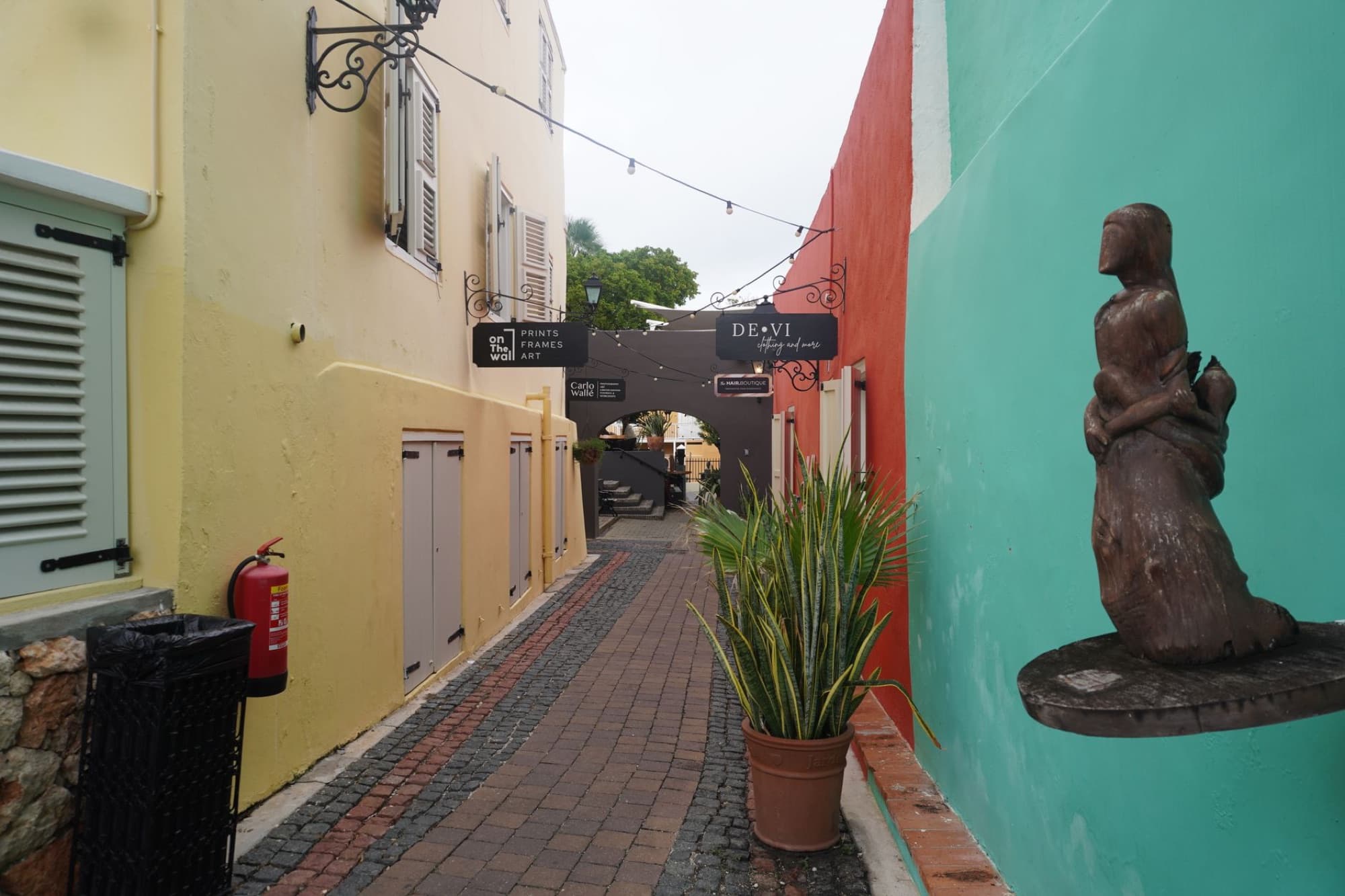 Charming alley in Willemstad, Curaçao featuring colorful walls and street art sculpture.