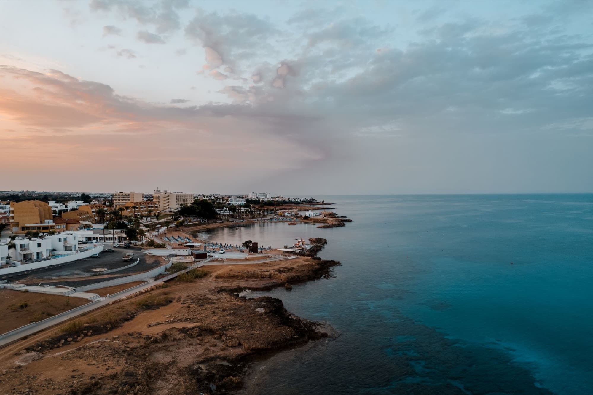 A stunning aerial shot of Protaras, Cyprus coastline with calm seas and a colorful sunset sky.