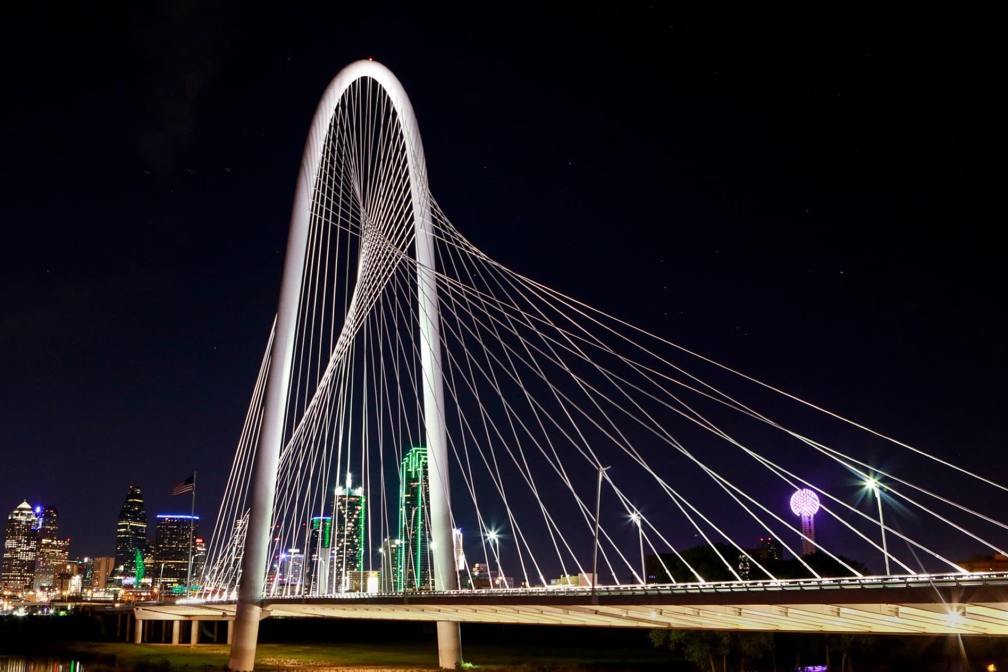 Stunning view of the Margaret Hunt Hill Bridge in Dallas with city skyline and vibrant lights at night.